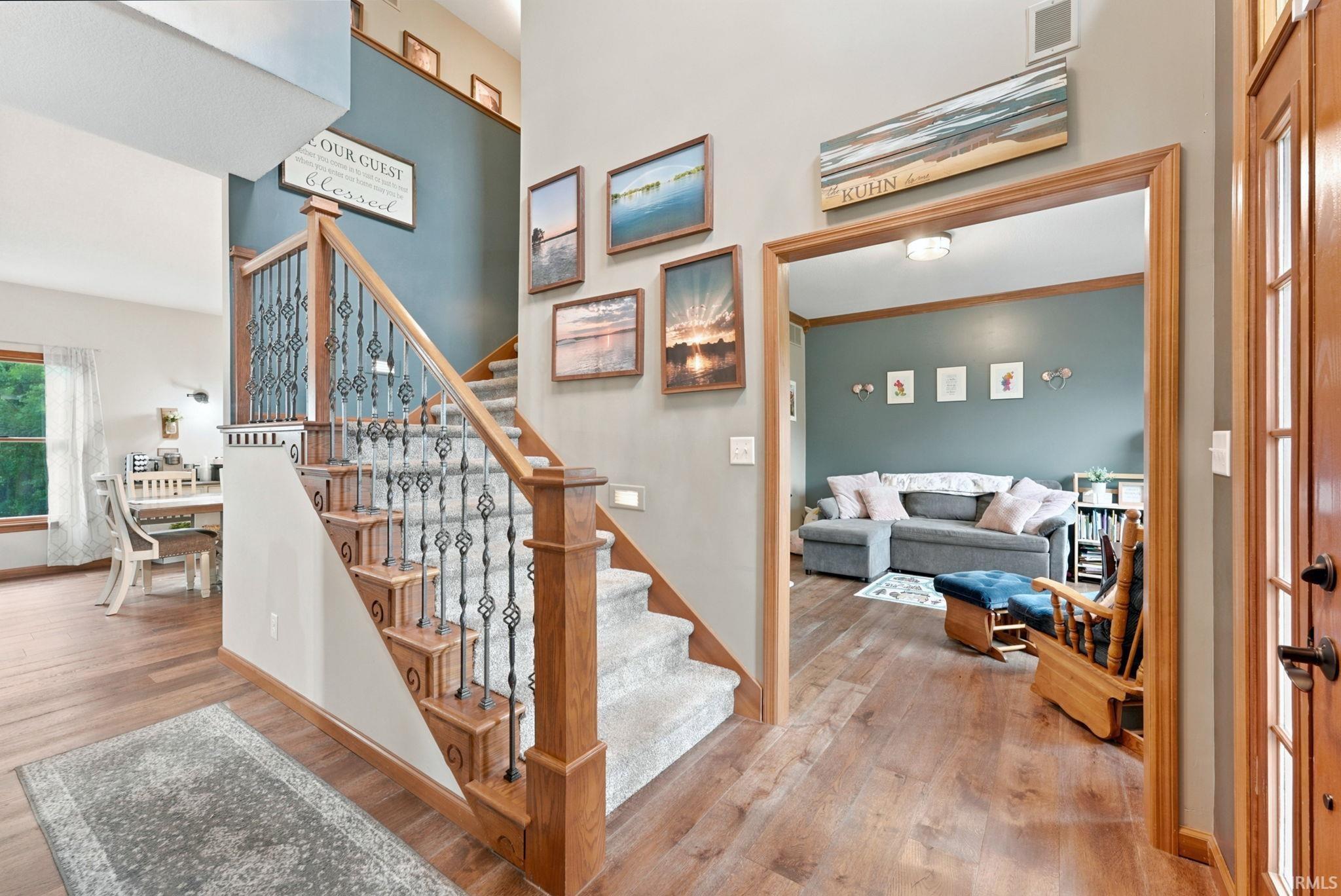 Image 1: Two-story entryway featuring wood-finish flooring, a carpeted staircase with ornate iron balusters, and a solid wood banister, Entrance Foyer Image 1: Two-story entryway featuring wood-finish flooring, a carpeted staircase with ornate iron balusters, and a solid wood banister, Entrance Foyer