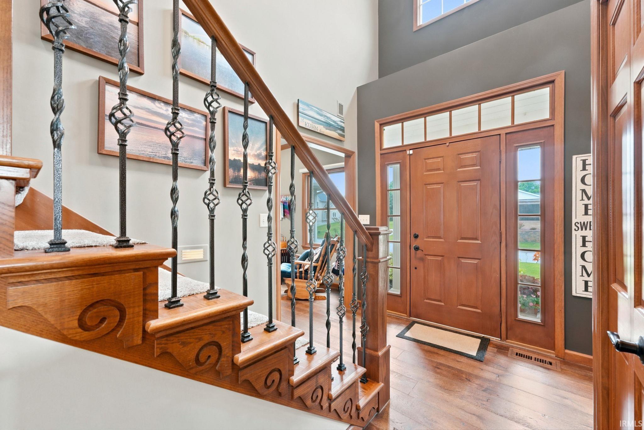 Image 2: Foyer featuring a hardwood entry door with sidelights and transom windows, wood-finish flooring, and a two-story ceiling, Entrance Foyer Image 2: Foyer featuring a hardwood entry door with sidelights and transom windows, wood-finish flooring, and a two-story ceiling, Entrance Foyer