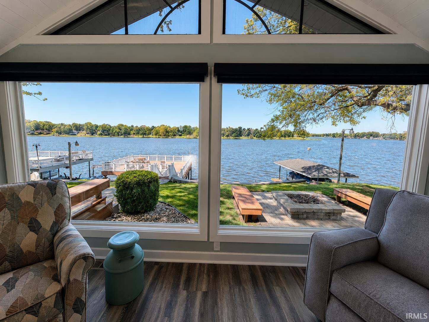 Image 1: Waterfront property featuring large windows, a stone fire pit with surrounding benches, a private dock, and wood-finish flooring, View Image 1: Waterfront property featuring large windows, a stone fire pit with surrounding benches, a private dock, and wood-finish flooring, View