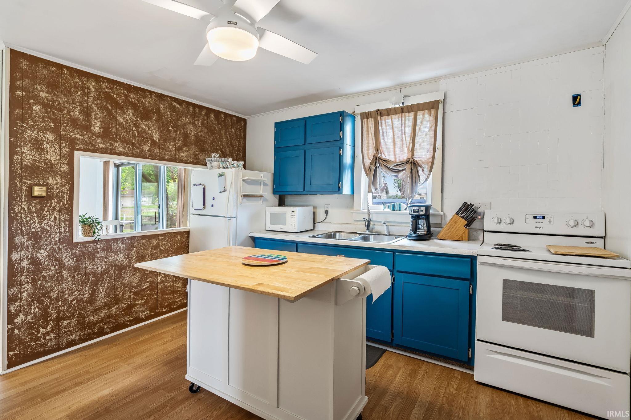 Image 2: Kitchen space featuring bold blue cabinetry, wood-finish flooring, and white appliances, Kitchen Image 2: Kitchen space featuring bold blue cabinetry, wood-finish flooring, and white appliances, Kitchen