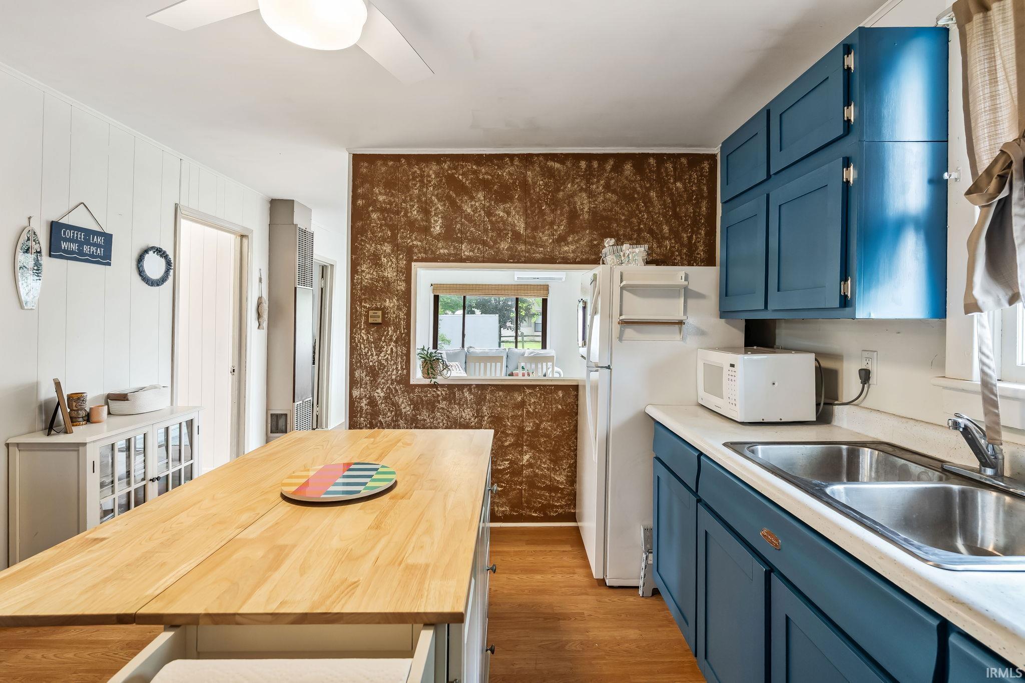 Image 3: Kitchen featuring a light wood island with built-in storage, contrasting blue cabinetry, a stainless steel double basin sink, and wood-finish flooring, Kitchen Image 3: Kitchen featuring a light wood island with built-in storage, contrasting blue cabinetry, a stainless steel double basin sink, and wood-finish flooring, Kitchen