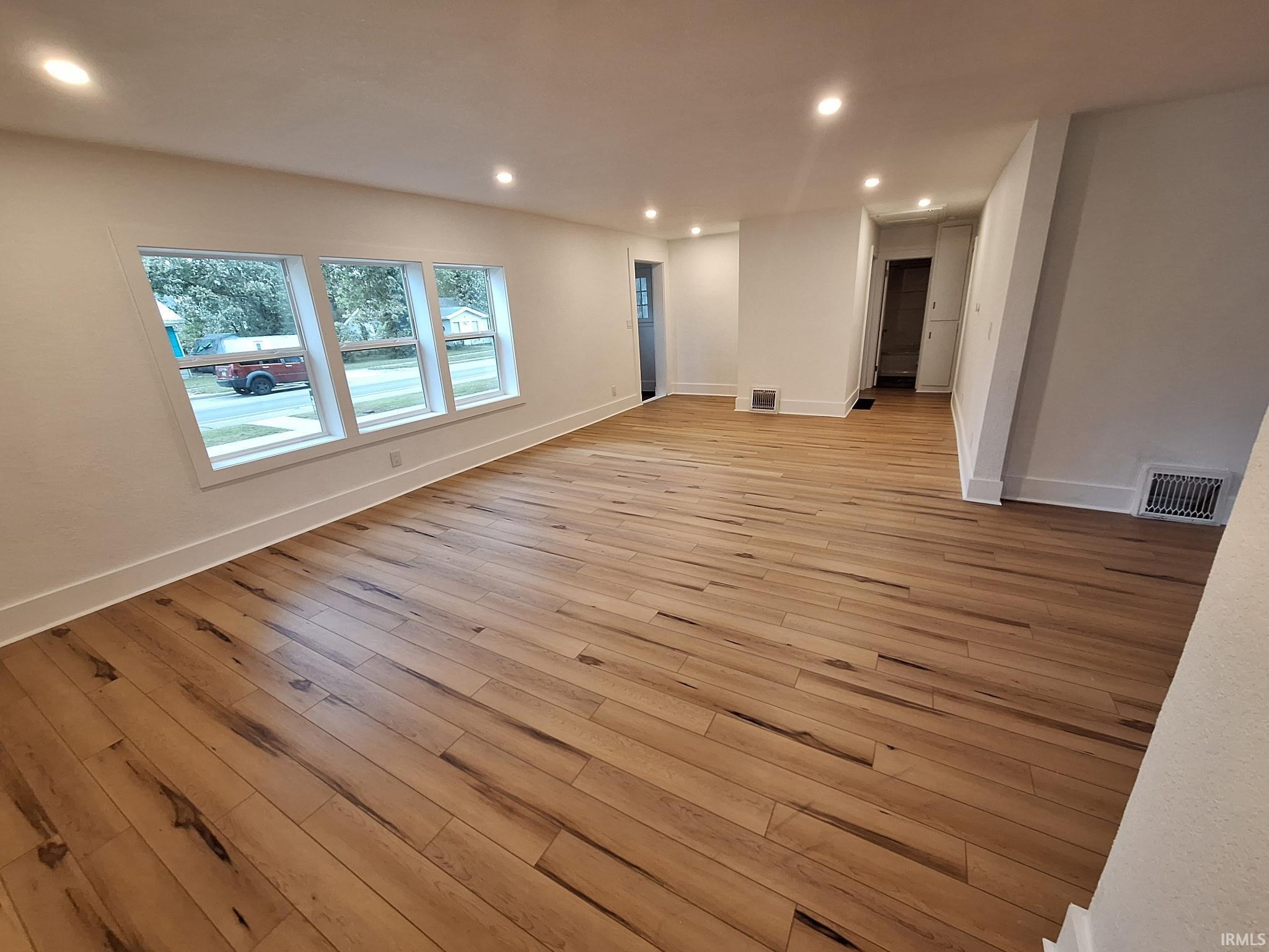 Image 4: Spacious living area featuring contemporary light wood-finish flooring, recessed ceiling lighting, three large windows with white trim, white baseboards, and white painted walls, Living Room