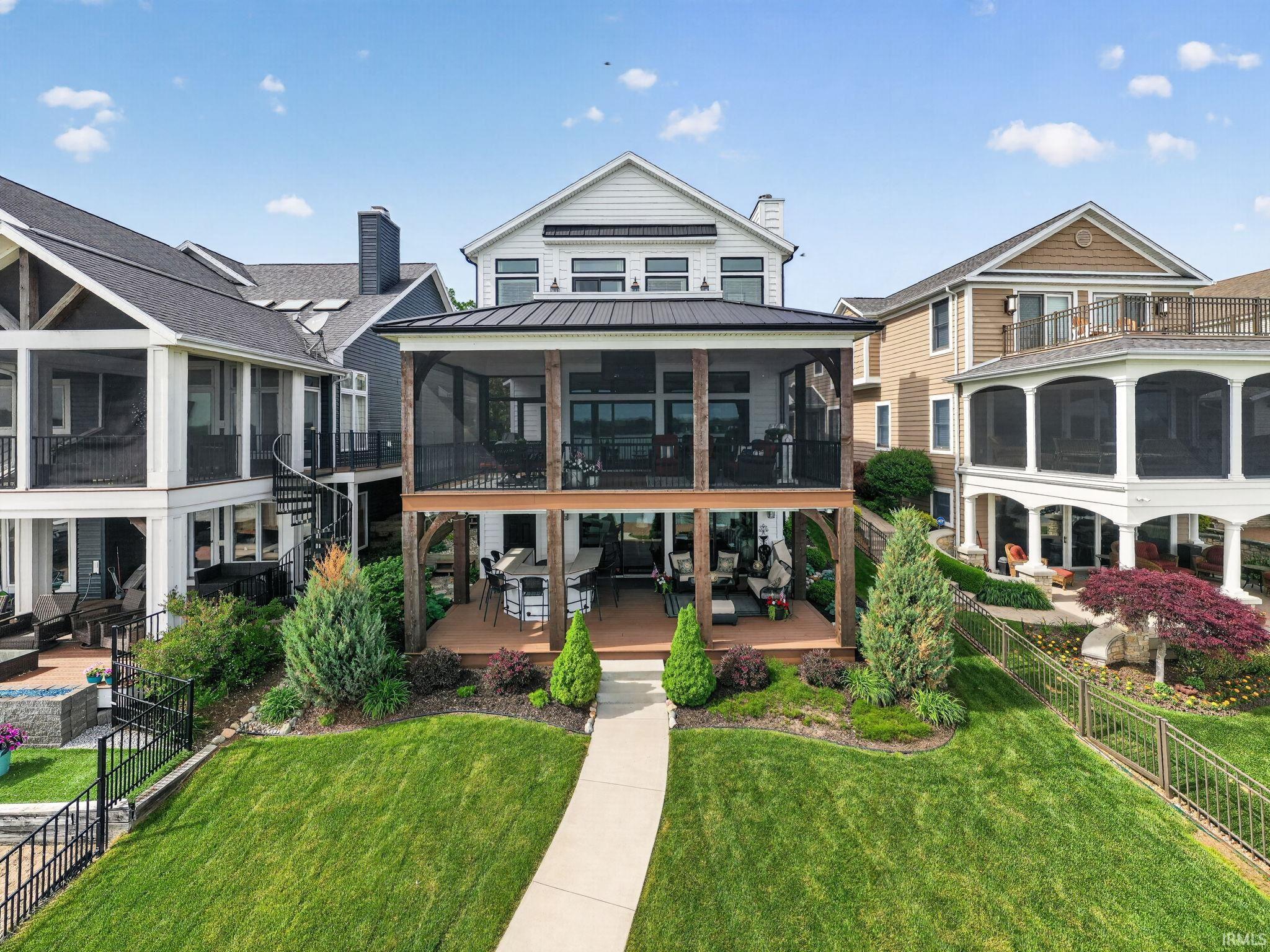 Image 0: Rear elevation featuring a double-story screened porch, an open-air deck, and a manicured lawn with a concrete pathway, Back Of Structure