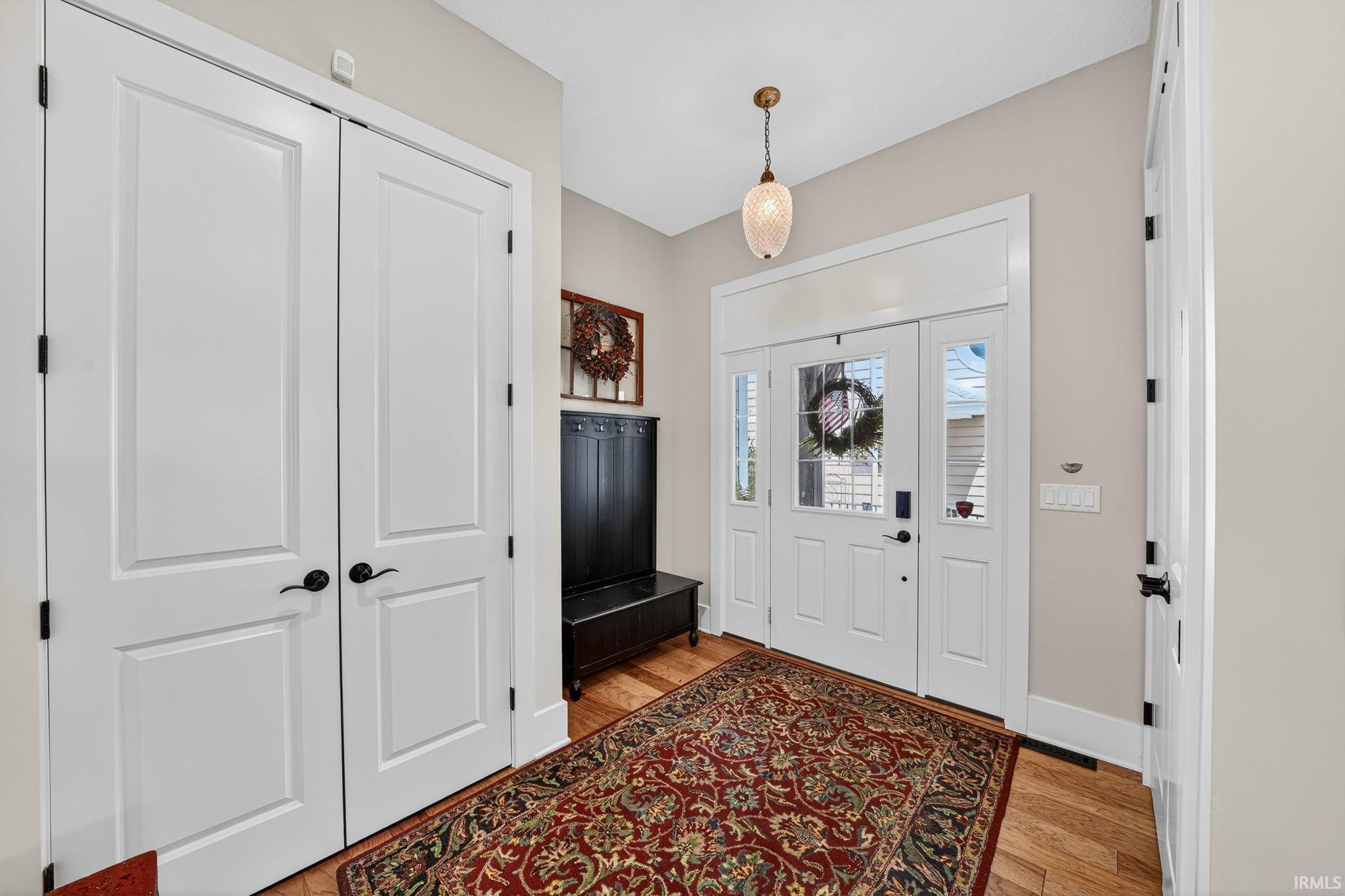 Image 2: Foyer featuring wood-finish flooring, a decorative pendant light fixture, and a white paneled entry door with sidelights, Entrance Foyer