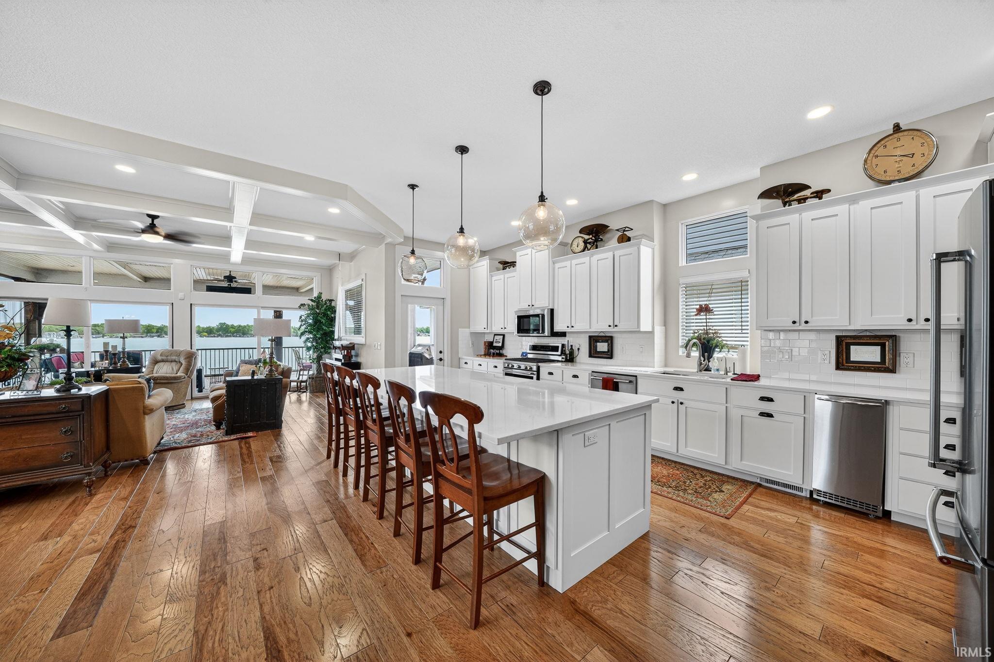 Image 3: Modern open-concept kitchen and living area featuring wood-finish flooring, white cabinetry, a large kitchen island with counter seating, stainless steel appliances, and a coffered ceiling, Kitchen