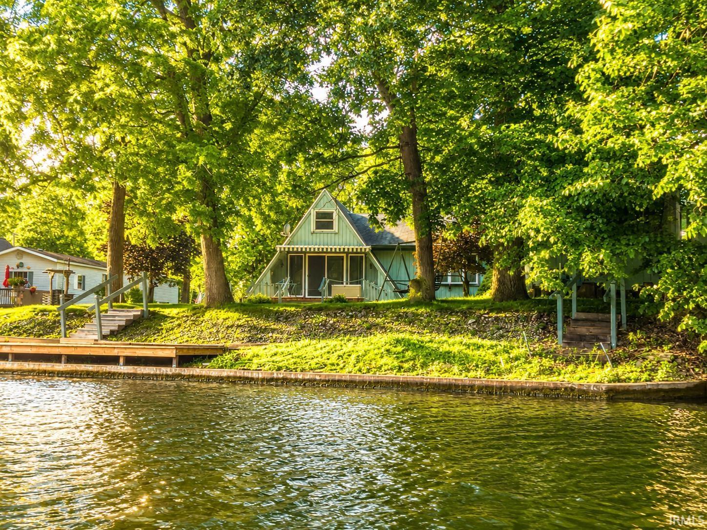 Image 1: Waterfront property featuring a wood dock, a sunsetter awning over the porch, a pitched roofline, and mature trees, View Image 1: Waterfront property featuring a wood dock, a sunsetter awning over the porch, a pitched roofline, and mature trees, View