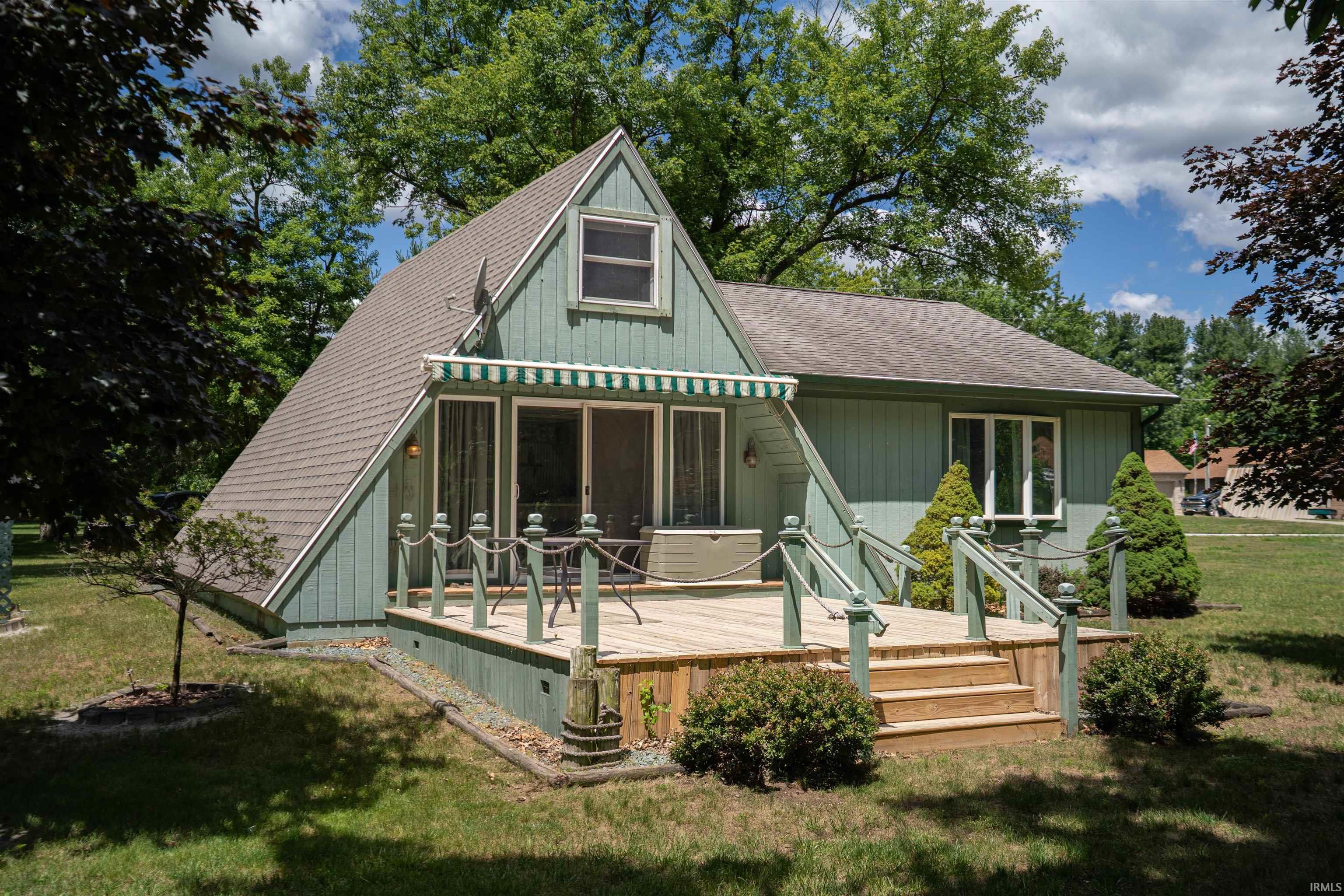 Image 2: A-frame home featuring a spacious wooden deck with baluster railing, a green and retracted white striped awning, and sliding glass doors, Back of Home Image 2: A-frame home featuring a spacious wooden deck with baluster railing, a green and retracted white striped awning, and sliding glass doors, Back of Home