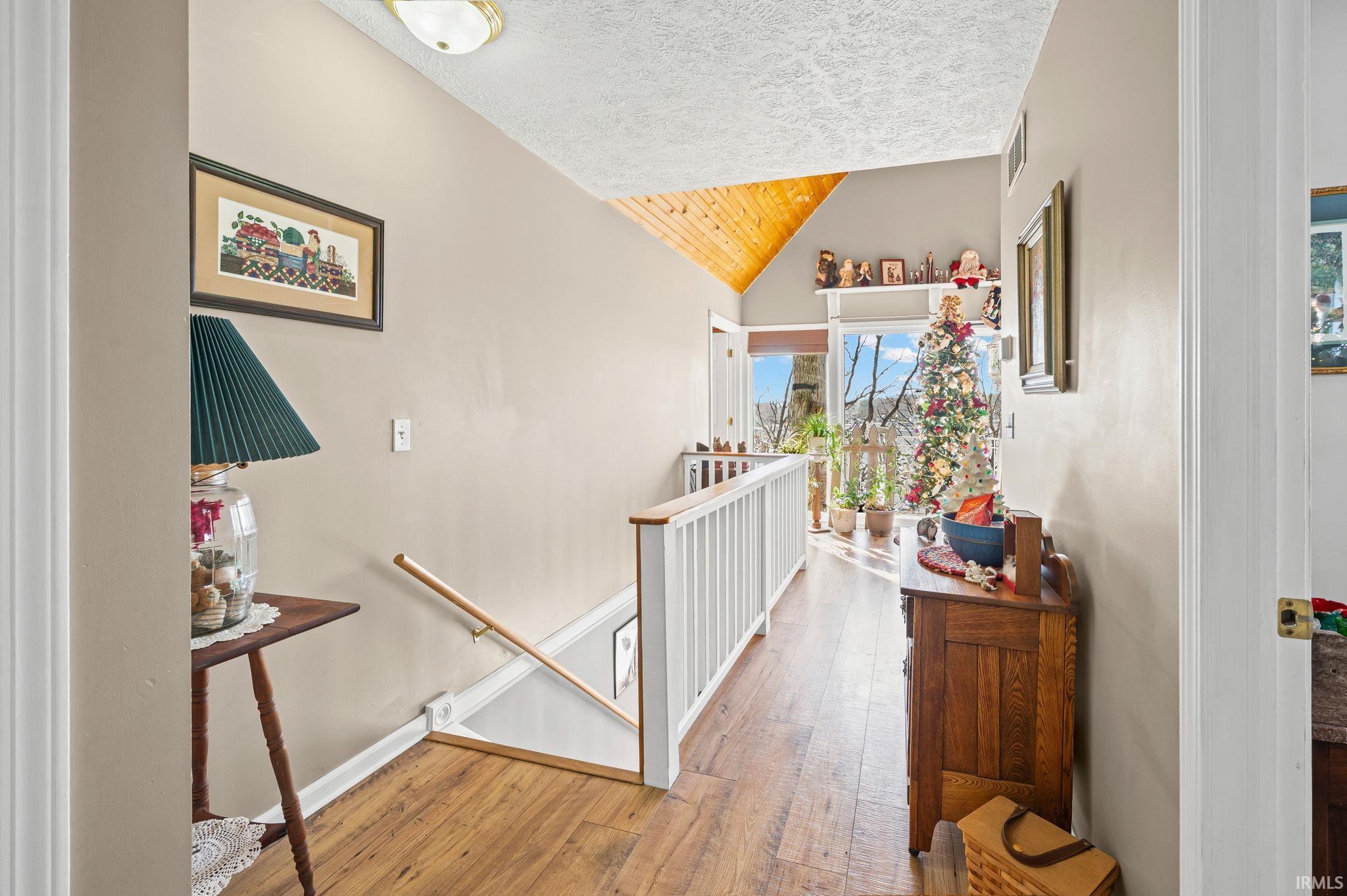 Image 2: Hall featuring an upstairs landing, vaulted ceiling, wood-type flooring, wooden ceiling, and a textured ceiling, Hallway