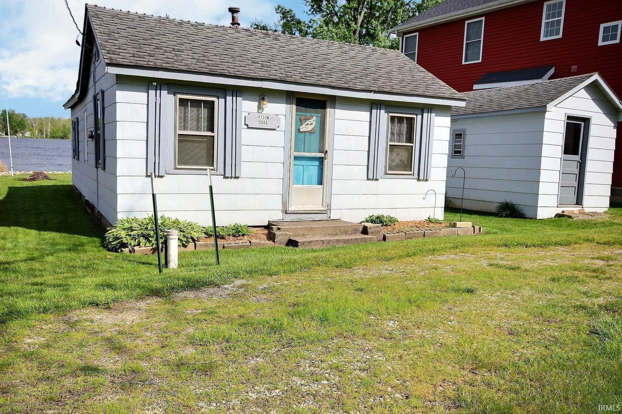 Image 0: Single-story home featuring light-colored siding, a dark shingled roof, and a vibrant blue front door, Front Of Structure Image 0: Single-story home featuring light-colored siding, a dark shingled roof, and a vibrant blue front door, Front Of Structure
