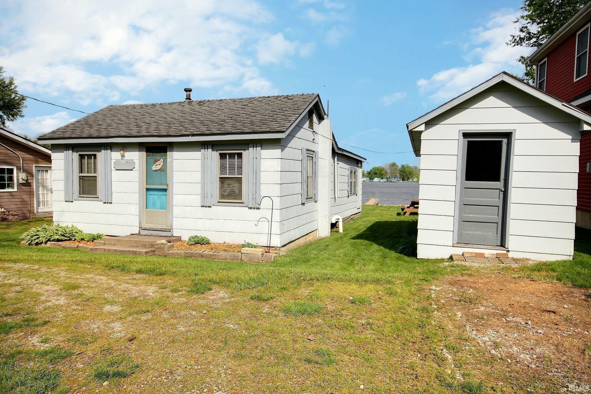 Image 2: White siding cottage featuring a gray shingle roof and a separate storage shed, View - Front Yard Image 2: White siding cottage featuring a gray shingle roof and a separate storage shed, View - Front Yard