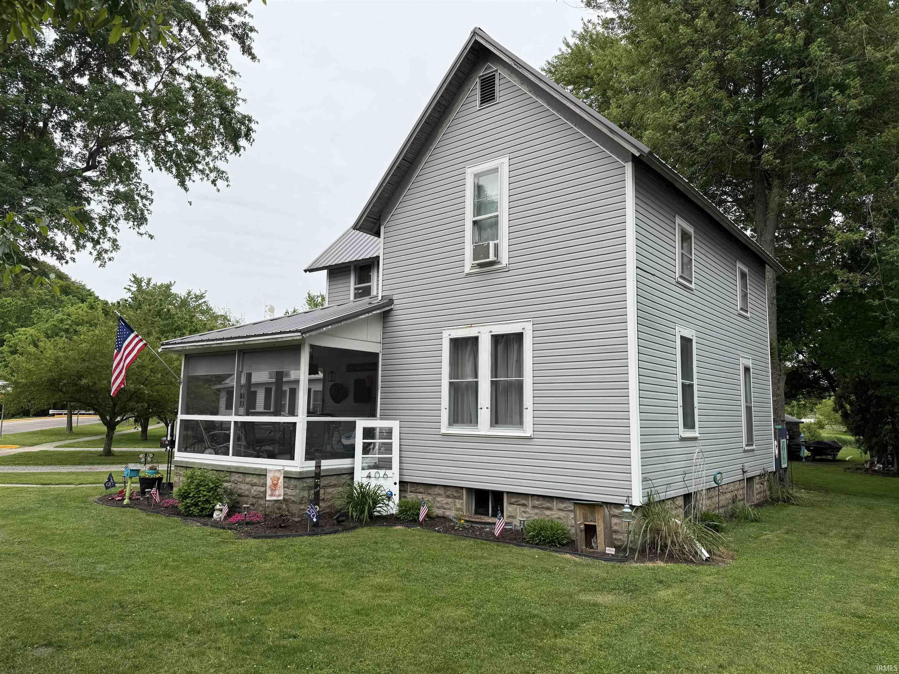 Image 2: Exterior featuring light gray siding, white trim, a screened-in porch with a metal roof, a stone foundation, and a verdant lawn, Front Of Structure Image 2: Exterior featuring light gray siding, white trim, a screened-in porch with a metal roof, a stone foundation, and a verdant lawn, Front Of Structure