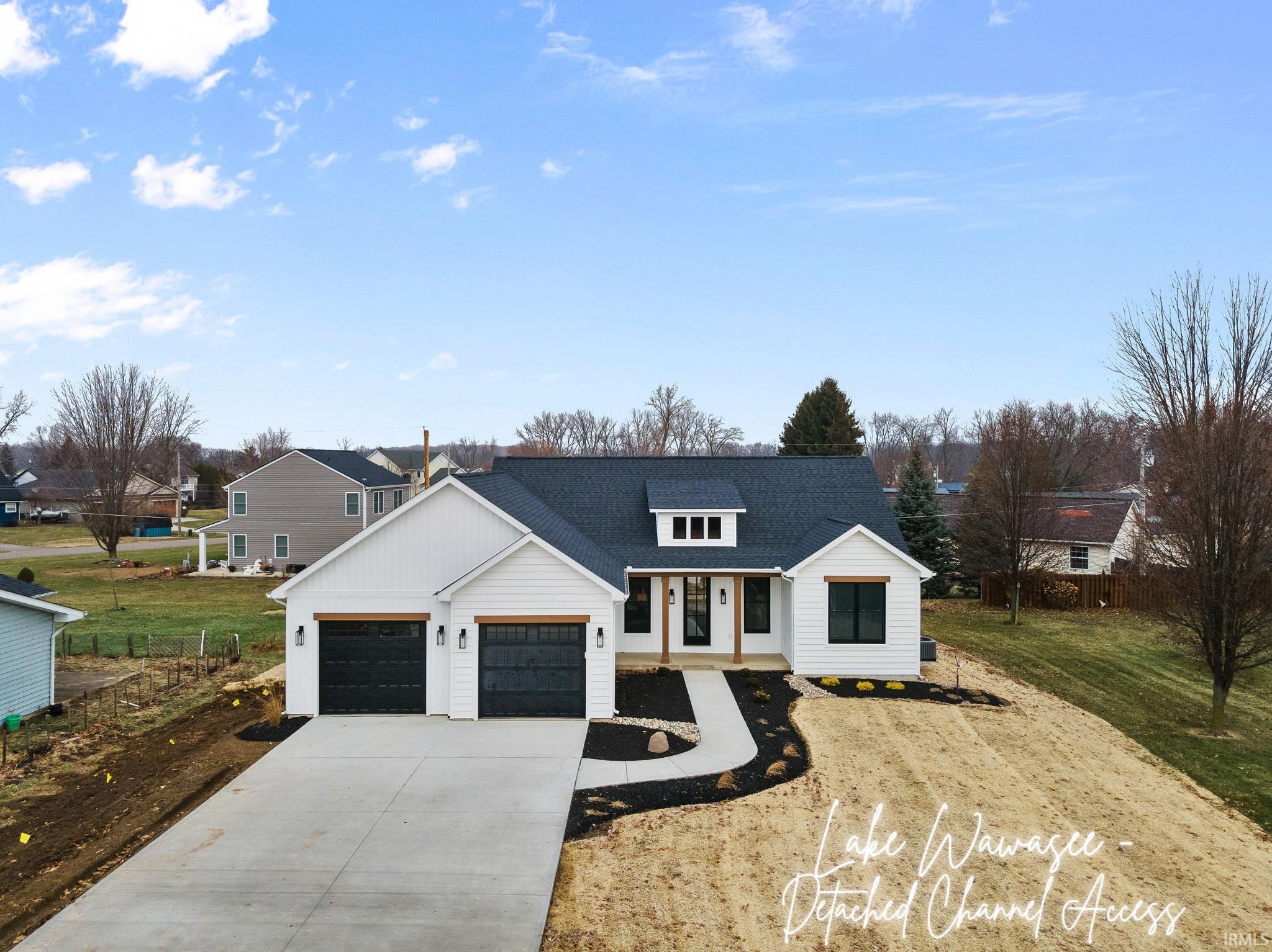 Image 3: Modern inspired farmhouse featuring large concrete driveway, natural wood accents, seeded yard, attached garage w/black doors and neutral trim details, Modern Farmhouse