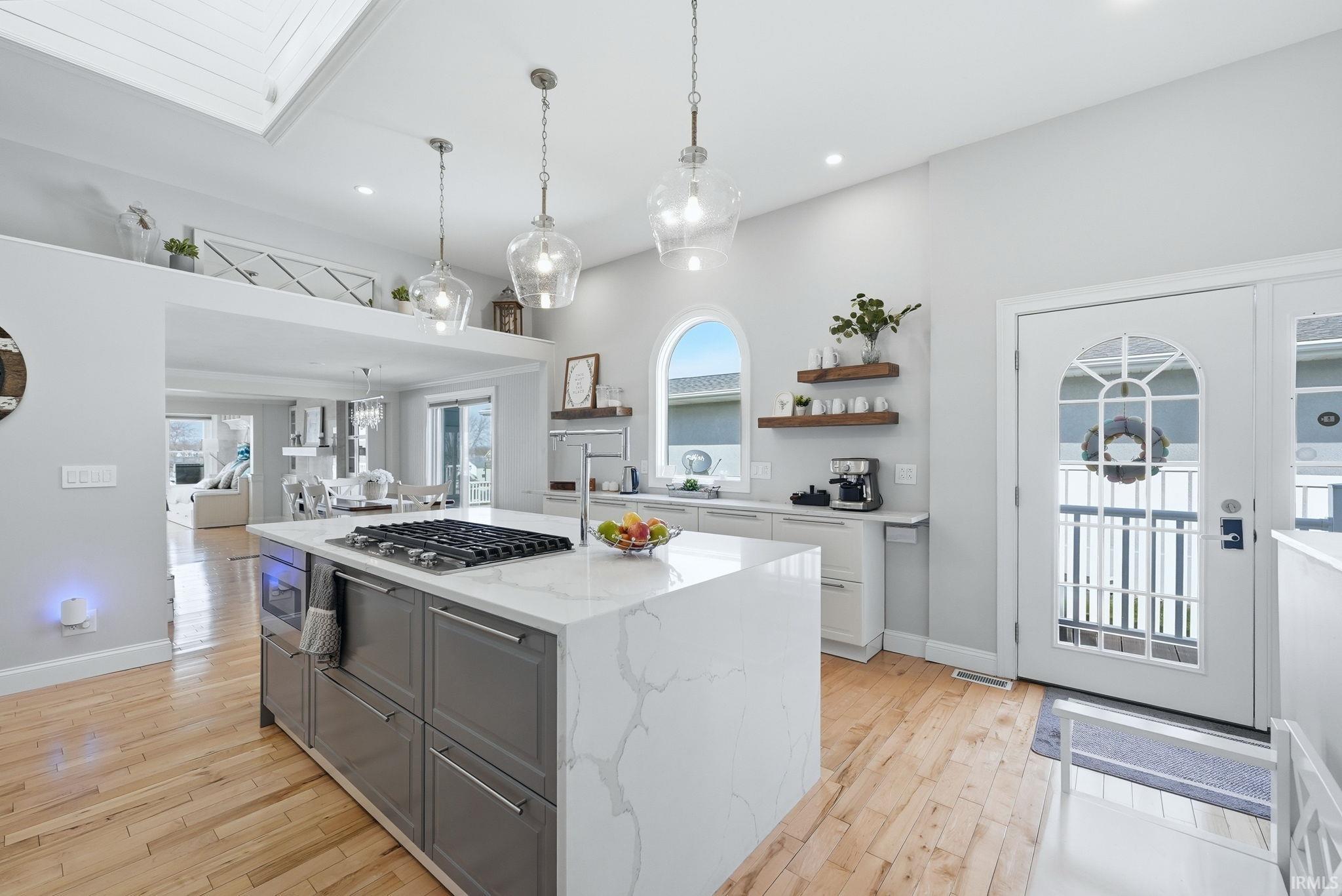 Image 1: Kitchen with light stone counters, gray cabinets, a kitchen island with sink, light wood-style floors, and open shelves, Kitchen