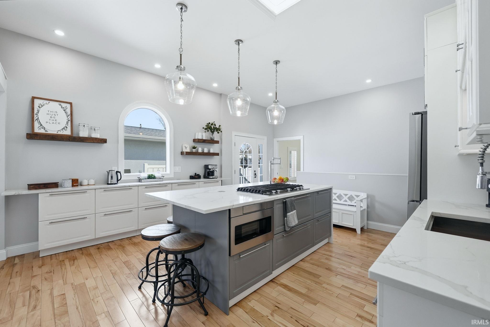 Image 2: Kitchen with light stone counters, a center island, open shelves, a kitchen breakfast bar, and light wood finished floors, Kitchen