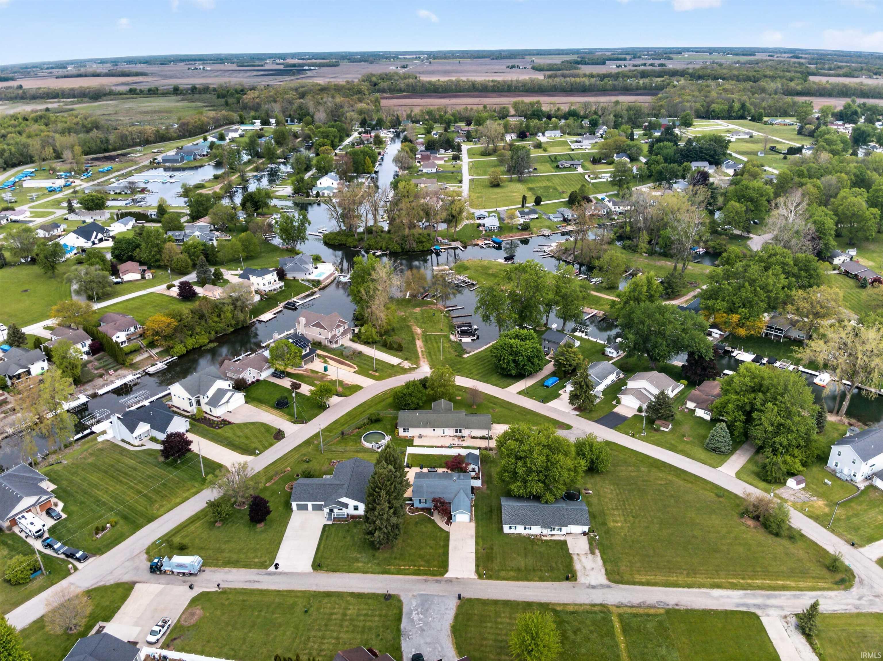 Image 1: Aerial perspective showcasing a residential area featuring multiple waterways, numerous detached homes, mature trees, and agricultural fields in the background, Aerial View Image 1: Aerial perspective showcasing a residential area featuring multiple waterways, numerous detached homes, mature trees, and agricultural fields in the background, Aerial View