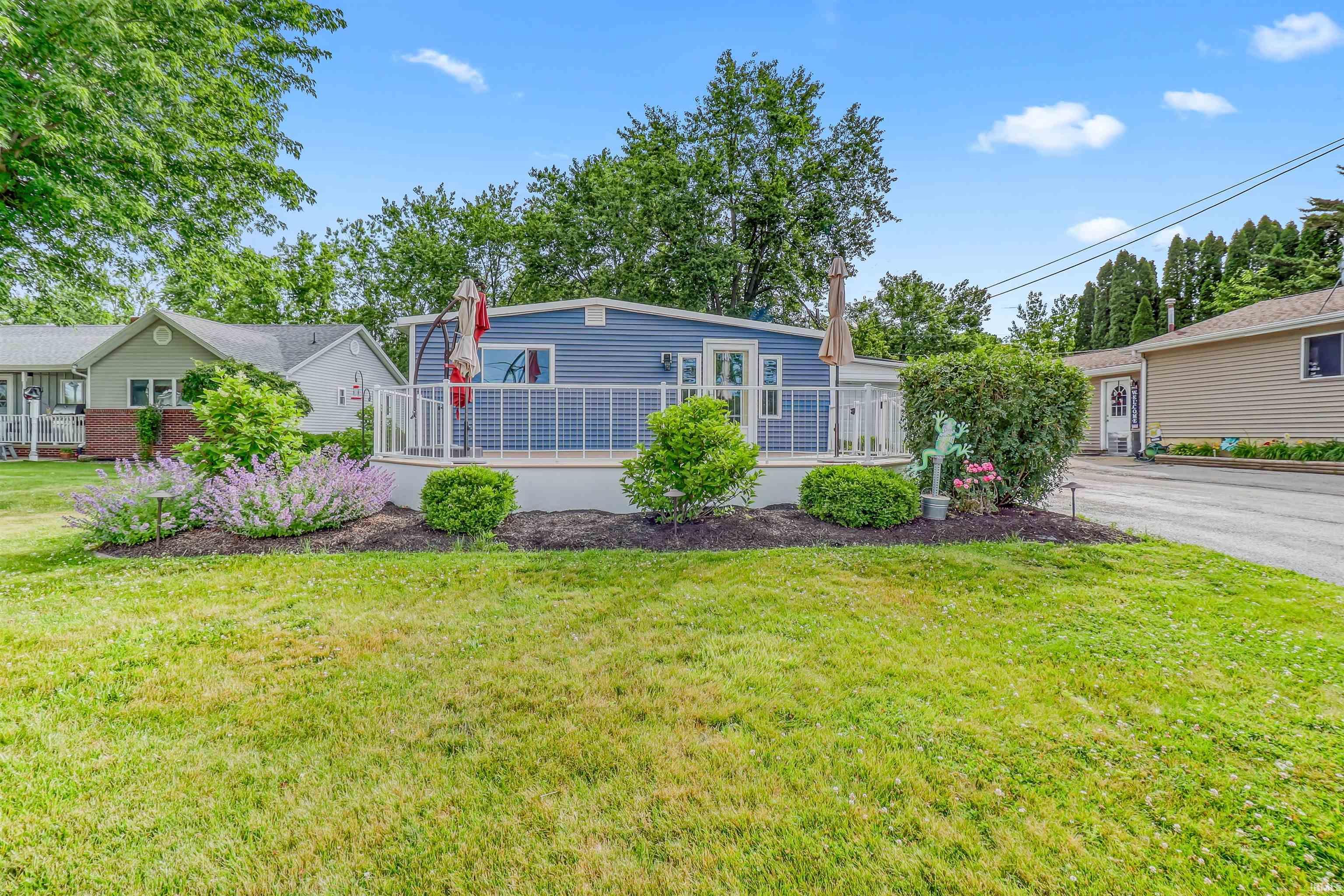 Image 1: Blue siding residence featuring a white-railed elevated deck, landscaped garden beds, and a grassy lawn, Front Of Structure Image 1: Blue siding residence featuring a white-railed elevated deck, landscaped garden beds, and a grassy lawn, Front Of Structure