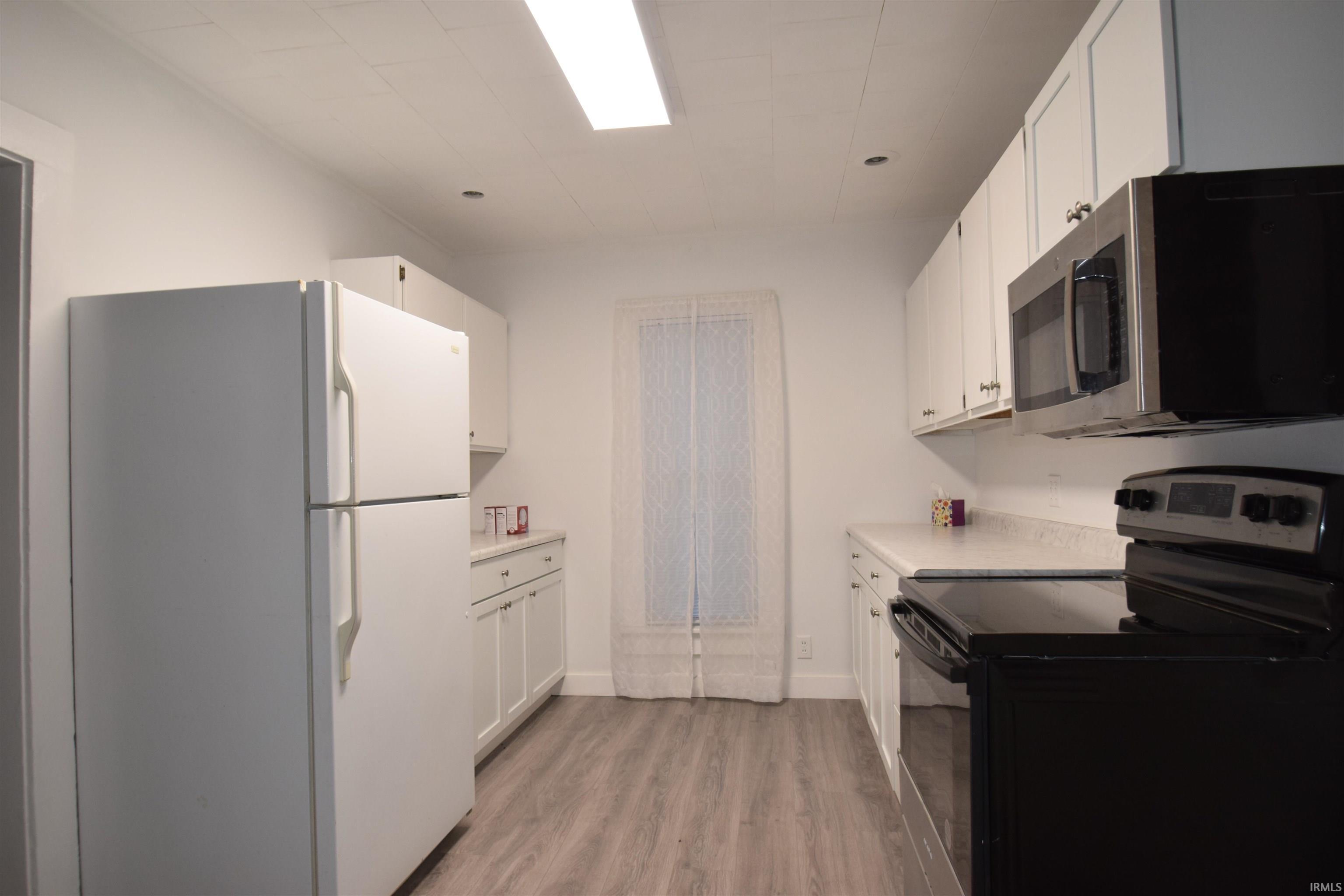 Image 3: Kitchen featuring black electric range, freestanding refrigerator, light countertops, stainless steel microwave, and white cabinets, Kitchen