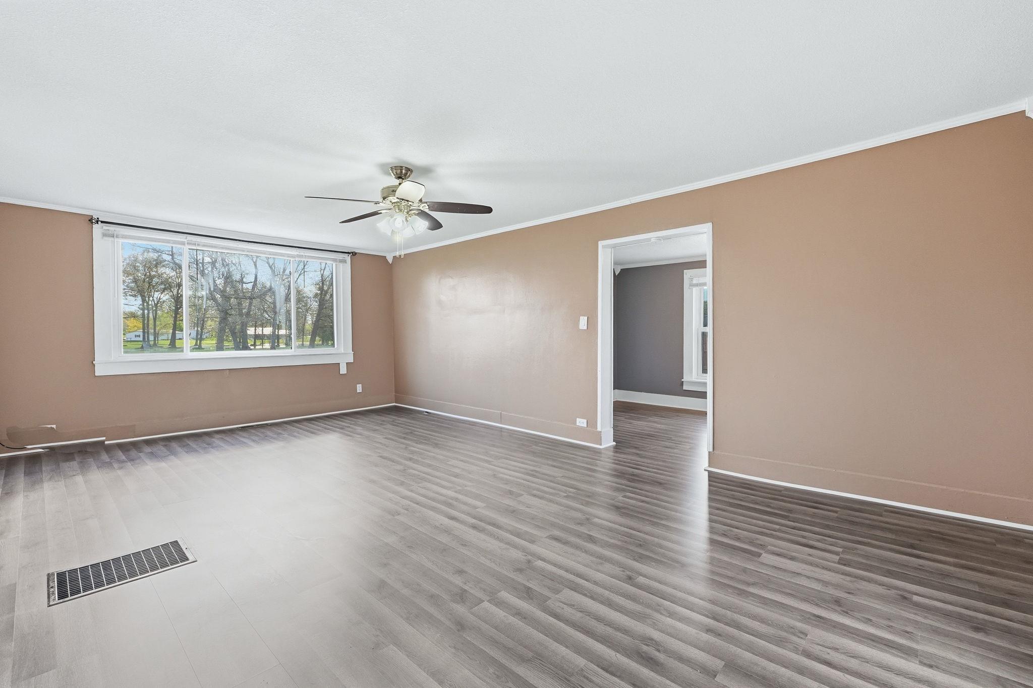Image 2: Spacious room featuring wood-finish flooring, a large window, a ceiling fan, and an open doorway to an additional interior space, Other