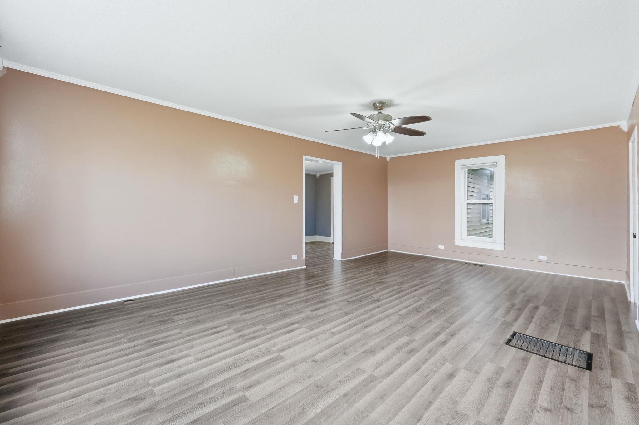 Image 3: Open-concept room featuring wood-finish flooring, a ceiling fan with integrated lighting, a single pane window with white trim, and light beige walls with white baseboards and crown molding, Other