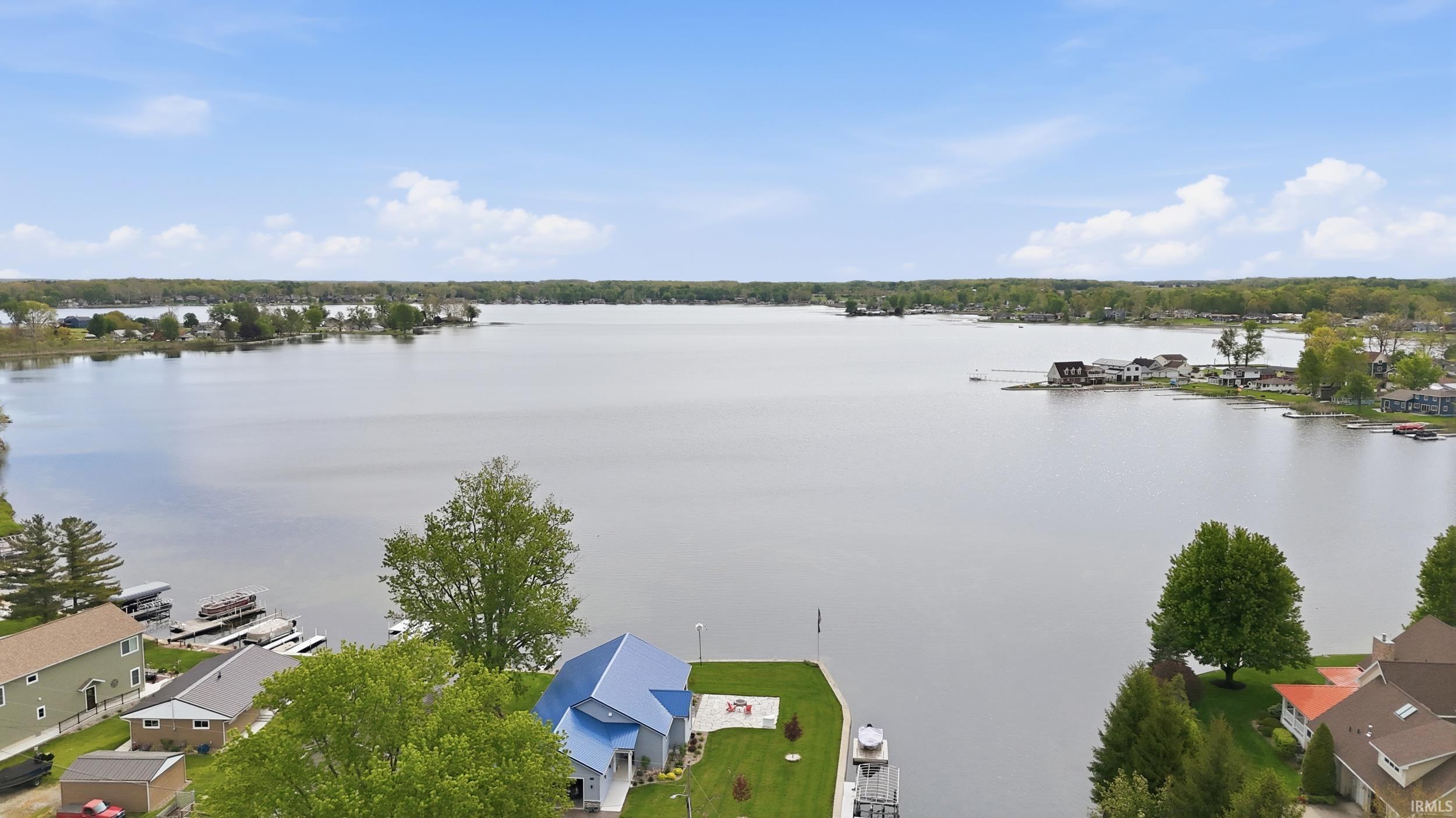 Image 3: Waterfront property featuring a contemporary home with a blue metal roof, private dock, lush green lawn, and mature trees, Aerial View Image 3: Waterfront property featuring a contemporary home with a blue metal roof, private dock, lush green lawn, and mature trees, Aerial View