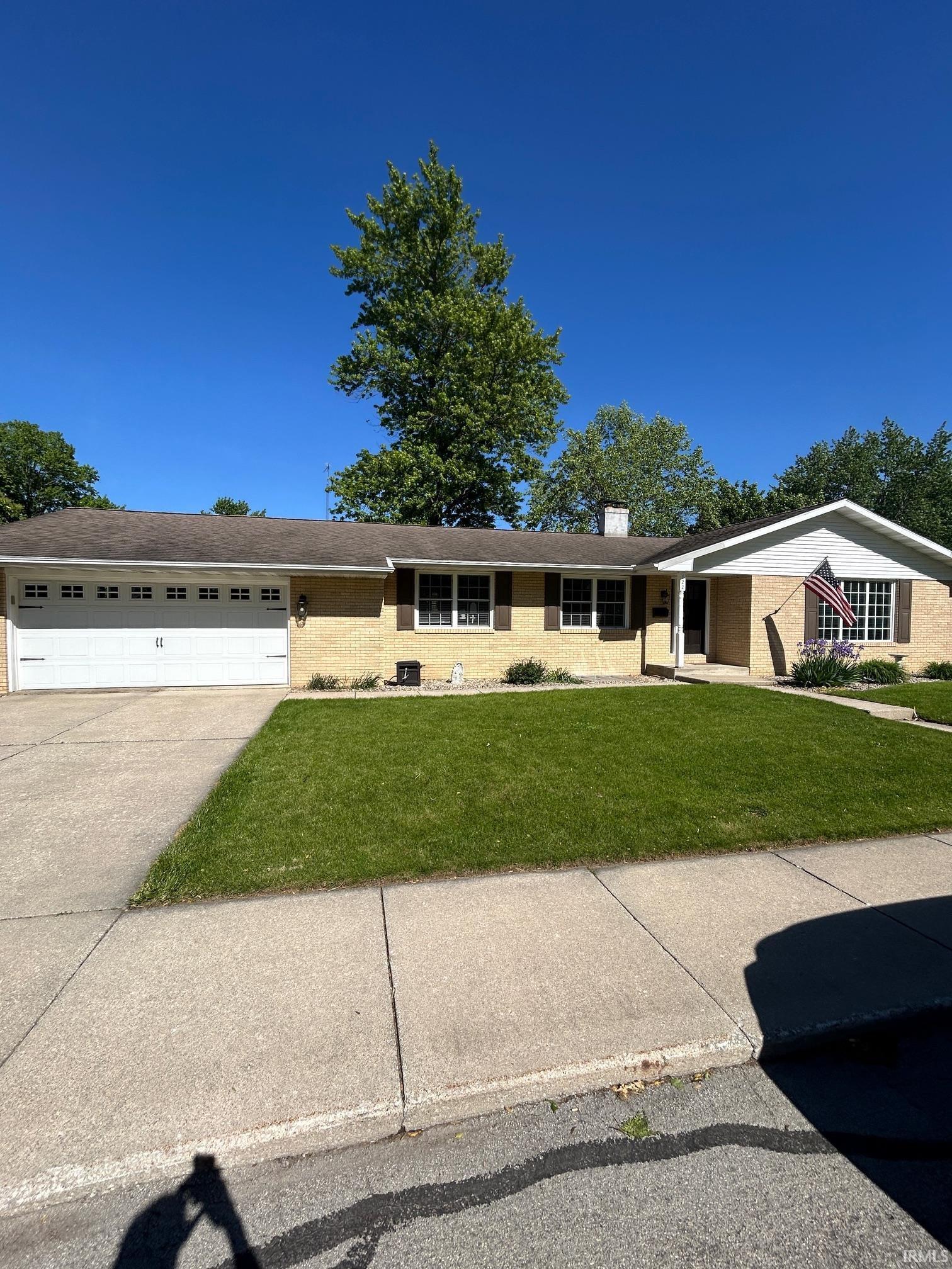 Image 0: Ranch-style residence featuring a light brick exterior, a two-car garage with a white door, and dark window shutters, Front Of Structure Image 0: Ranch-style residence featuring a light brick exterior, a two-car garage with a white door, and dark window shutters, Front Of Structure