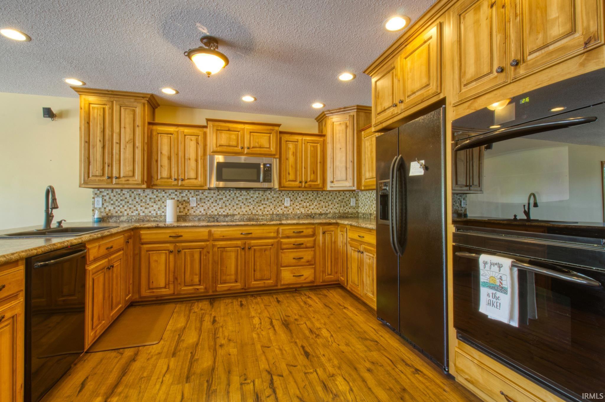 Image 1: Kitchen featuring abundant wood cabinetry, wood-finish flooring, granite countertops, and a mosaic tile backsplash, Kitchen Image 1: Kitchen featuring abundant wood cabinetry, wood-finish flooring, granite countertops, and a mosaic tile backsplash, Kitchen