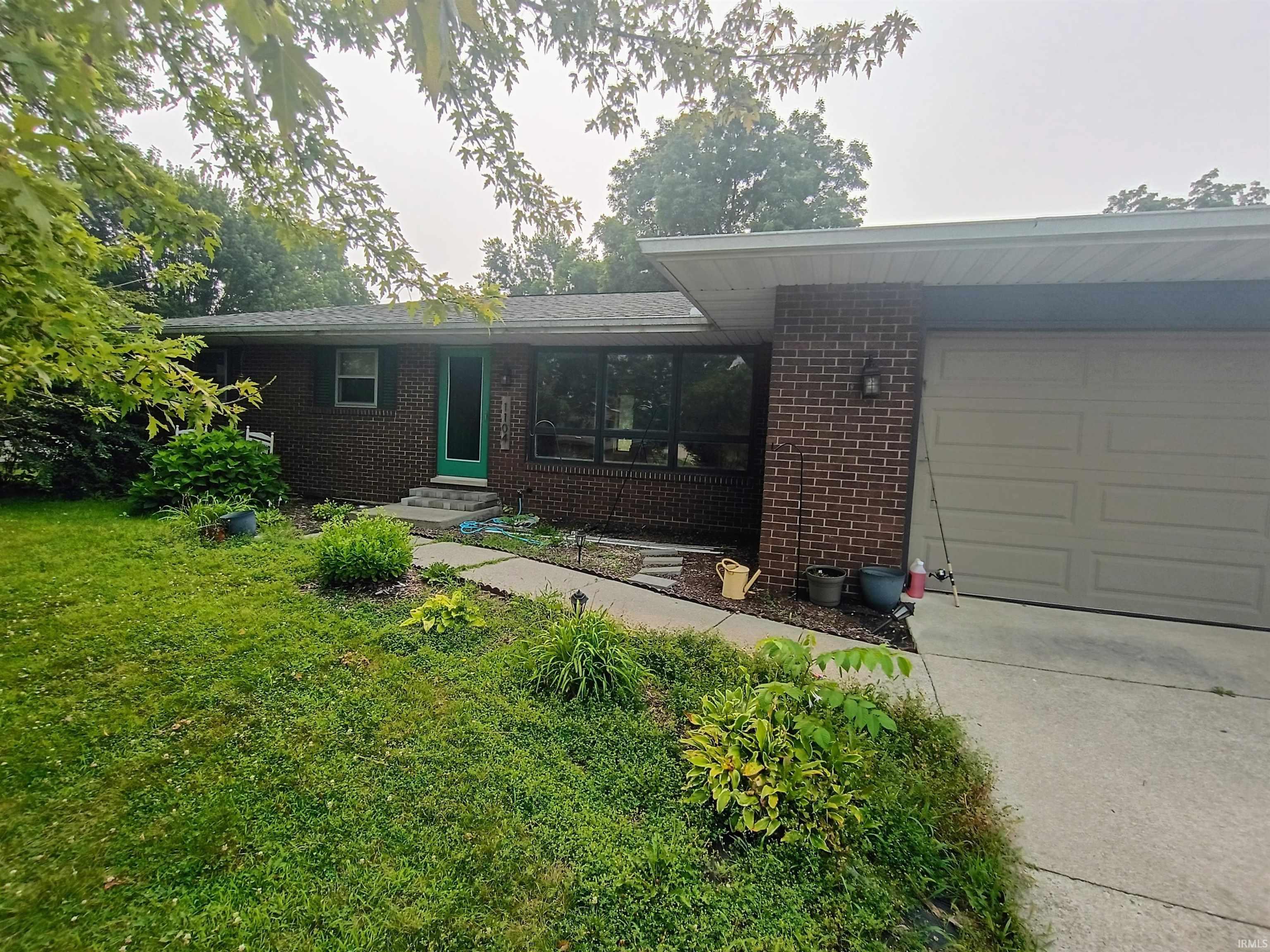 Image 0: Brick exterior residence featuring a green entry door, large front windows, and an attached garage, Front Of Structure Image 0: Brick exterior residence featuring a green entry door, large front windows, and an attached garage, Front Of Structure