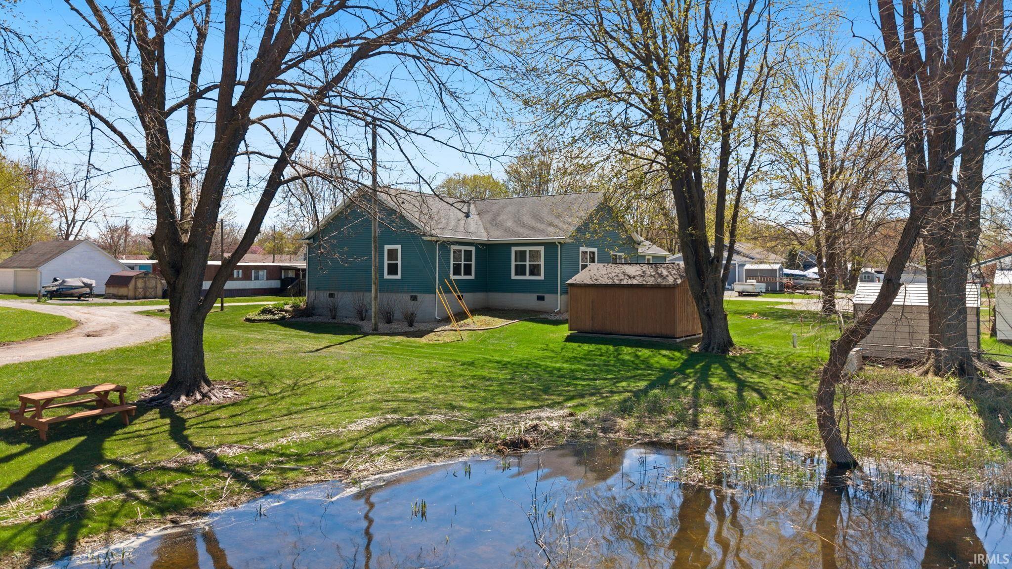 Image 2: Spacious property featuring a single-story residence with teal siding, a shingled roof, and white-framed windows, Back Of Structure