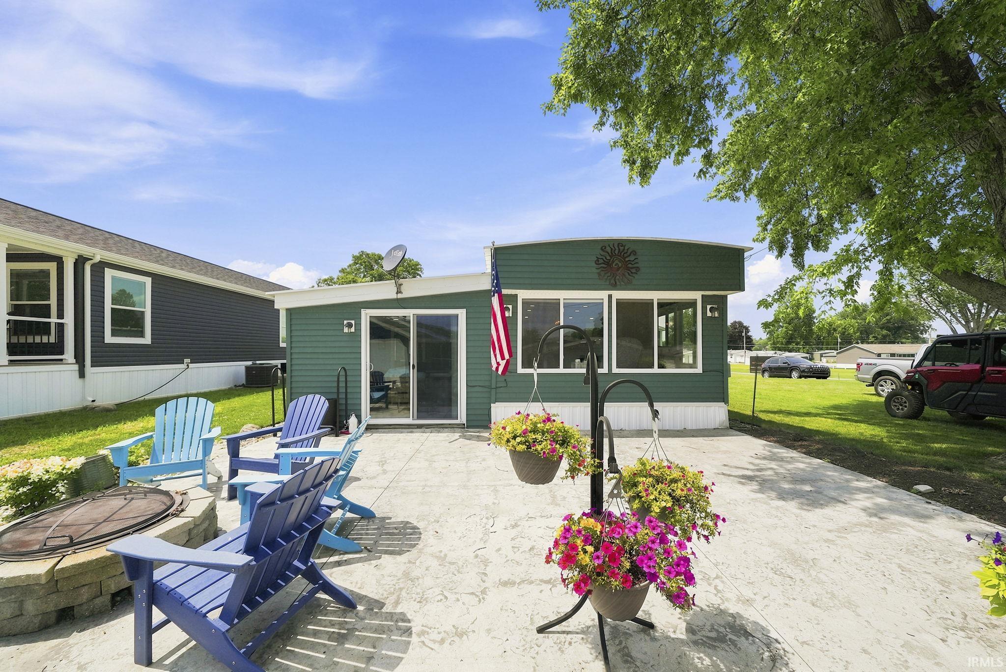 Image 2: Expansive concrete patio featuring a built-in stone fire pit, sliding glass doors, multiple windows, and a green siding exterior, Back Of Structure Image 2: Expansive concrete patio featuring a built-in stone fire pit, sliding glass doors, multiple windows, and a green siding exterior, Back Of Structure