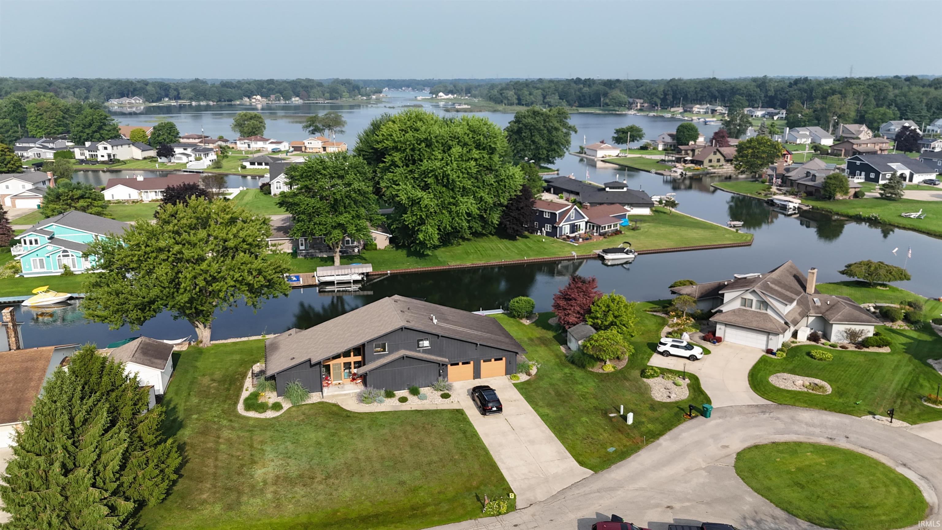 Image 1: Waterfront property featuring a dark-toned residence with a two-car garage, established landscaping, a private boat dock, and direct canal access, Aerial View Image 1: Waterfront property featuring a dark-toned residence with a two-car garage, established landscaping, a private boat dock, and direct canal access, Aerial View