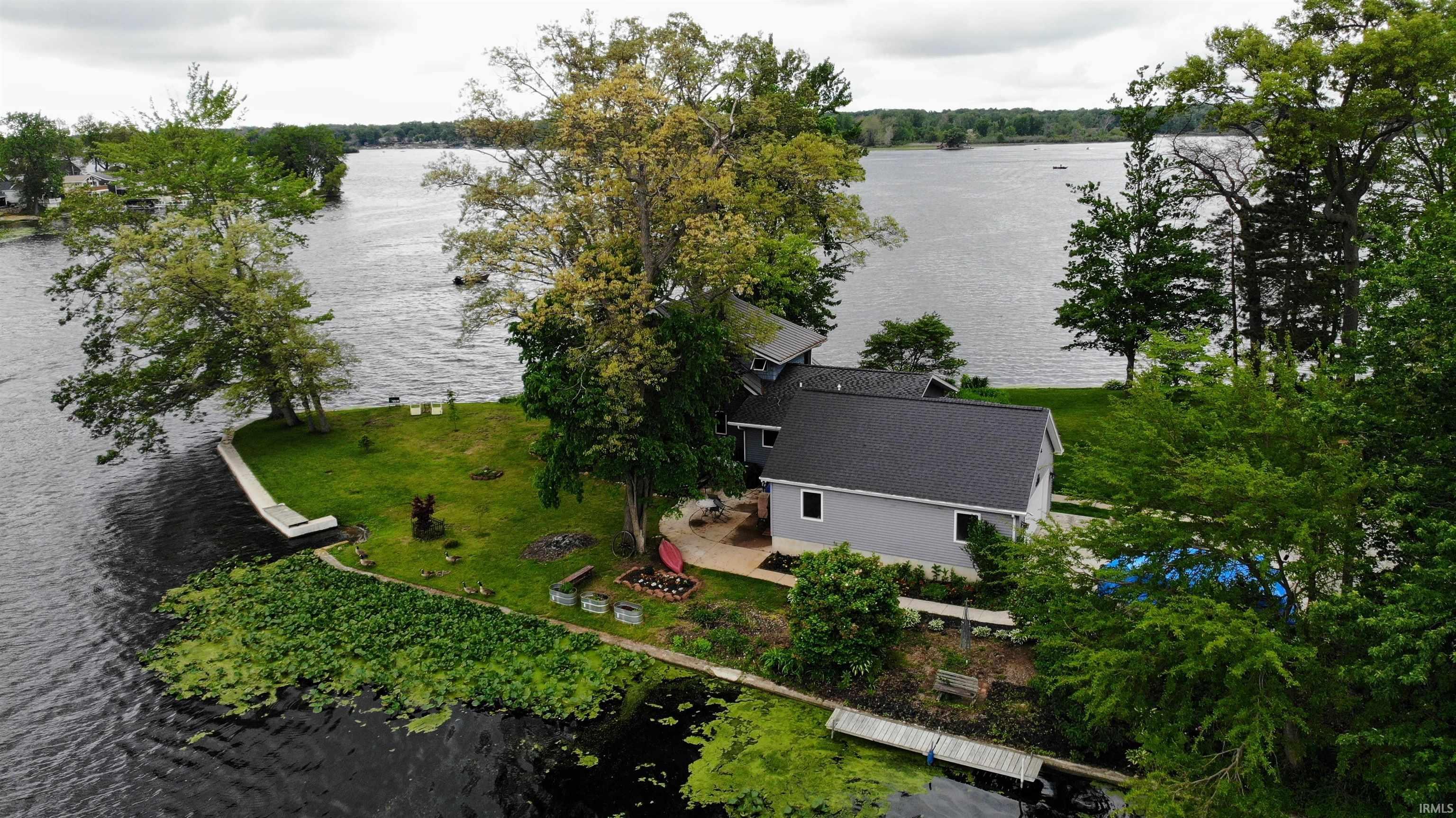 Image 1: Waterfront property featuring a gray exterior, dark shingle roof, mature trees, a private dock, and a manicured lawn, Aerial View