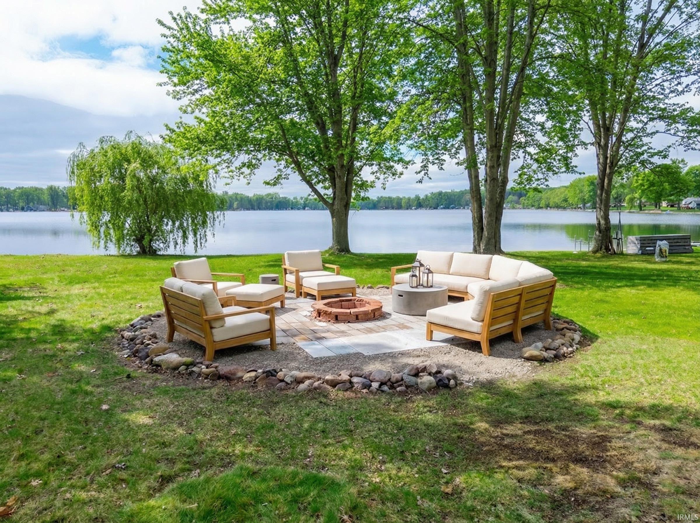 Image 2: View of grassy yard with a water view, an outdoor living space with a fire pit, and a patio area, Lakefront firepit with virtual staging Image 2: View of grassy yard with a water view, an outdoor living space with a fire pit, and a patio area, Lakefront firepit with virtual staging