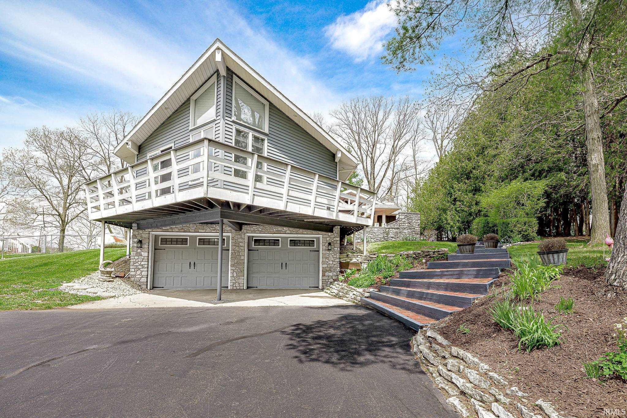 Image 2: A-frame home featuring a multi-level deck, two-car garage with stone-finish facade, and a terraced stone retaining wall with integrated steps, Front Of Structure