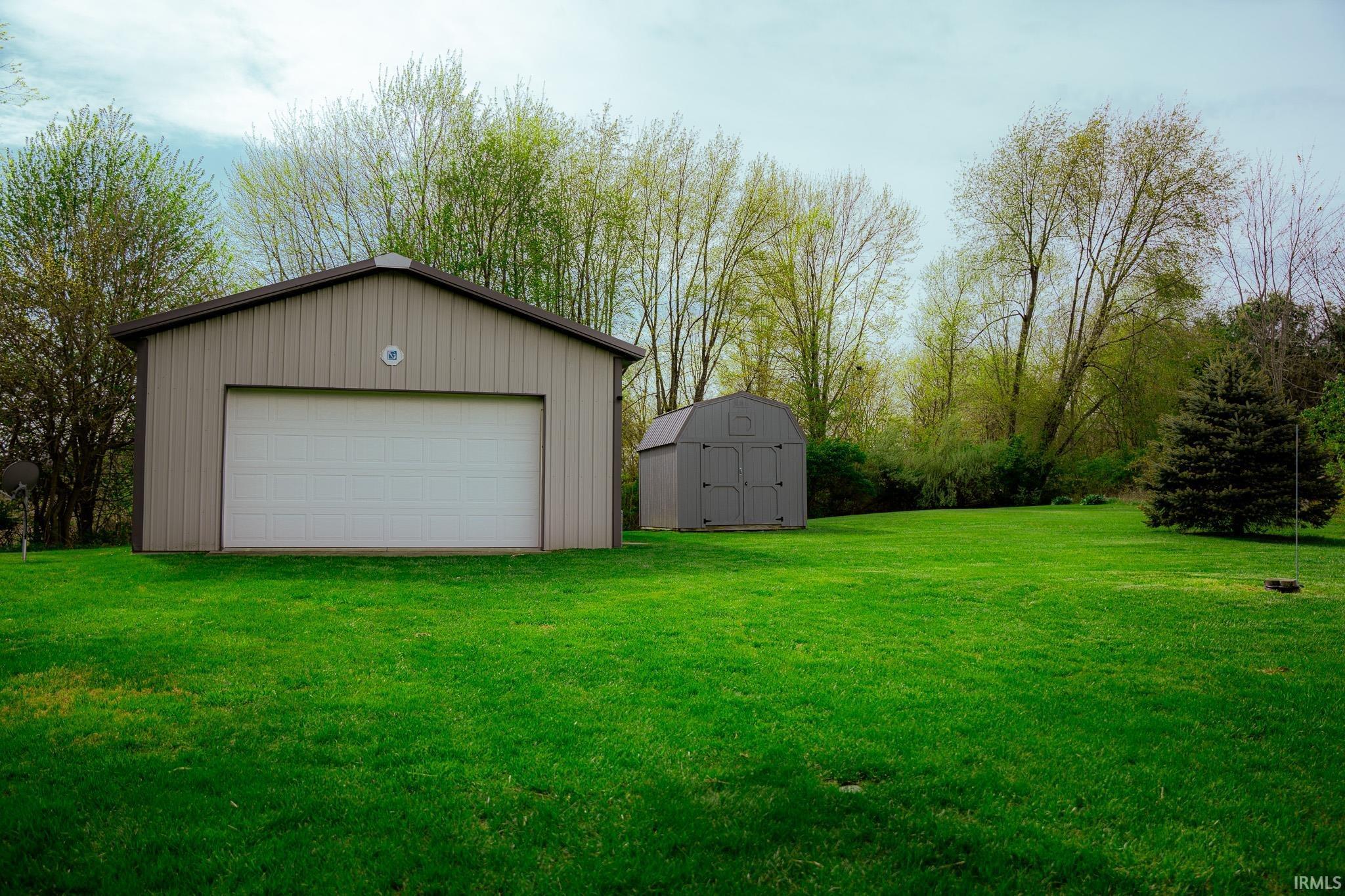 Image 2: Spacious yard featuring a large metal utility building with a white garage door, accompanied by a smaller storage shed, Outbuilding