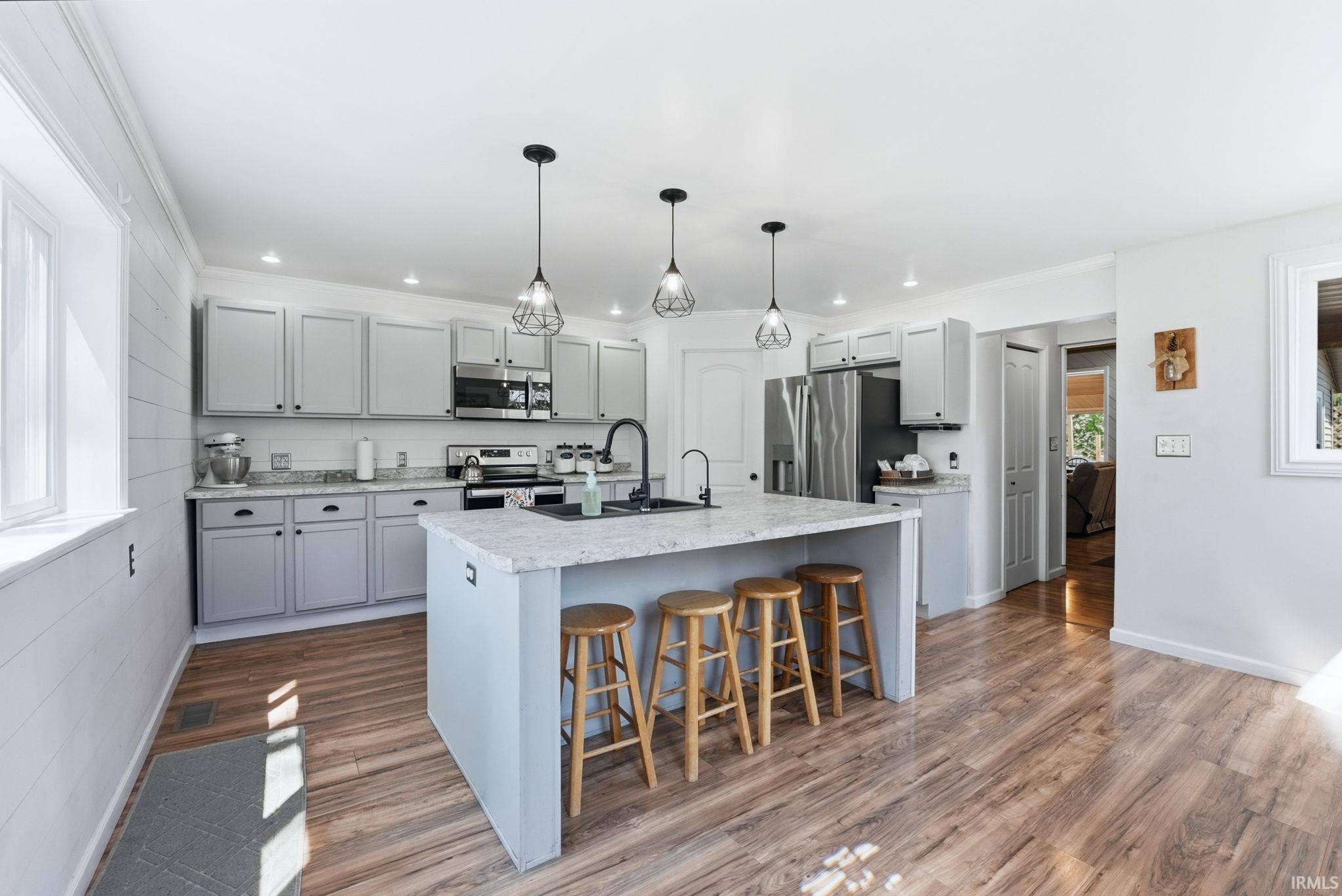 Image 3: Spacious kitchen featuring an island with seating, light gray cabinetry, stainless steel appliances, wood-finish flooring, and recessed lighting, Kitchen