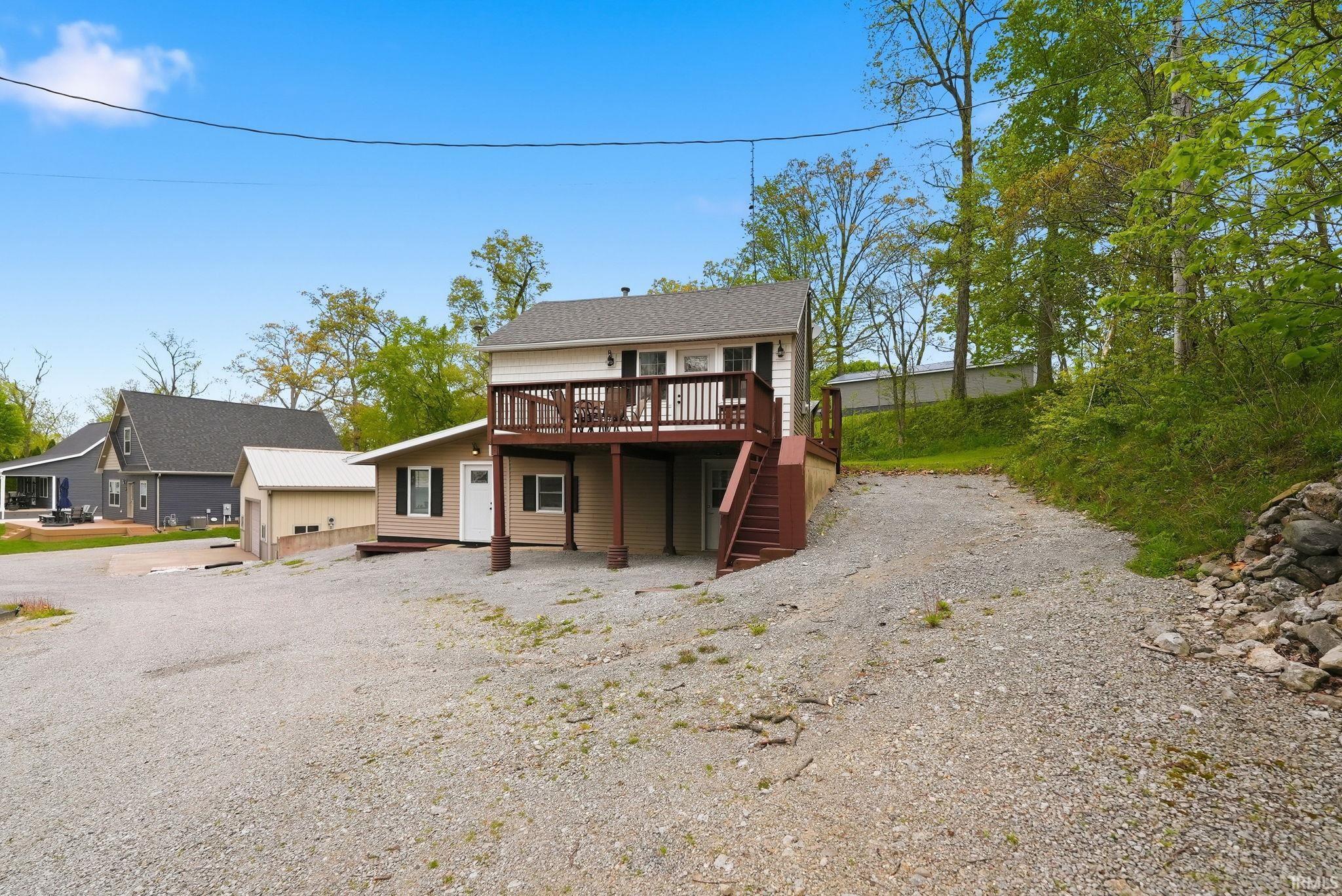 Image 2: Multi-level residence featuring a main entrance with a deck, an additional lower-level entry, and a gravel driveway, Front Of Structure Image 2: Multi-level residence featuring a main entrance with a deck, an additional lower-level entry, and a gravel driveway, Front Of Structure
