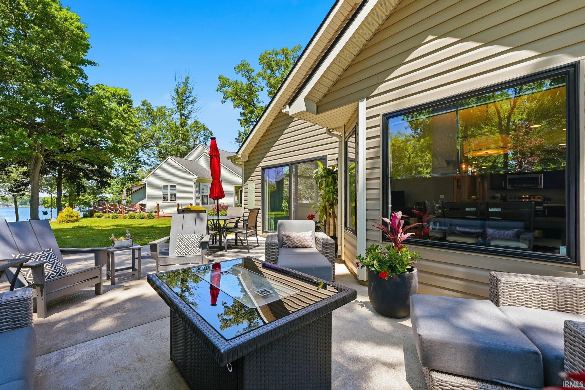 Image 1: Exterior patio with concrete hardscaping, large black-framed windows, beige siding, a glass-top fire pit, and a sliding glass door, Patio Image 1: Exterior patio with concrete hardscaping, large black-framed windows, beige siding, a glass-top fire pit, and a sliding glass door, Patio