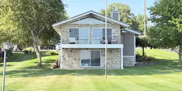 Image 2: Stone veneer exterior with a full-width upper balcony featuring cable railing, Lakeside View of Home