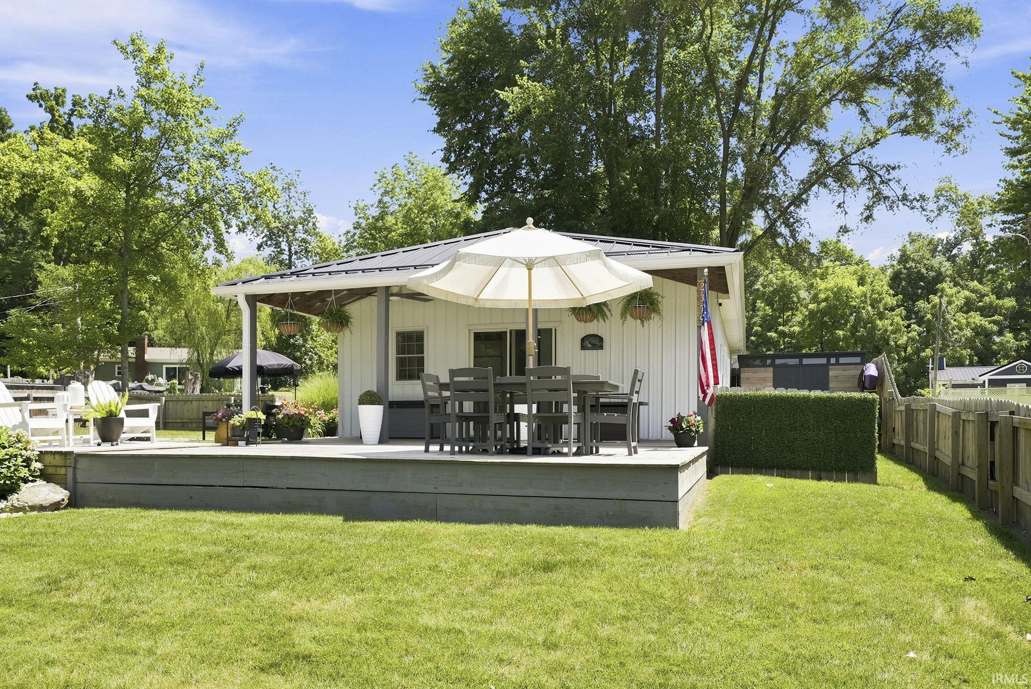 Image 1: Expansive backyard featuring a manicured lawn, a raised composite deck, and a white board-and-batten exterior structure with a covered porch, Back Of Structure Image 1: Expansive backyard featuring a manicured lawn, a raised composite deck, and a white board-and-batten exterior structure with a covered porch, Back Of Structure