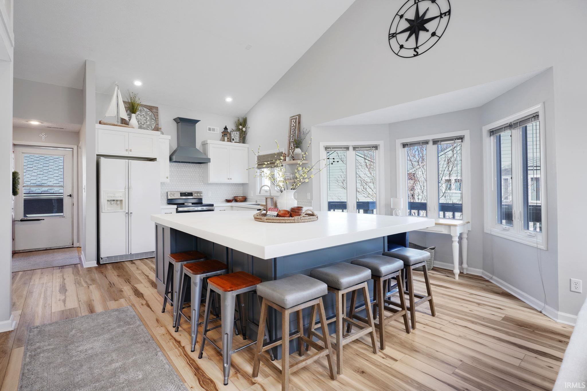 Image 3: Two tone kitchen with two tone cabinetry, a breakfast bar area, white refrigerator with ice dispenser, light wood-style flooring, and vaulted ceiling, Kitchen Image 3: Two tone kitchen with two tone cabinetry, a breakfast bar area, white refrigerator with ice dispenser, light wood-style flooring, and vaulted ceiling, Kitchen