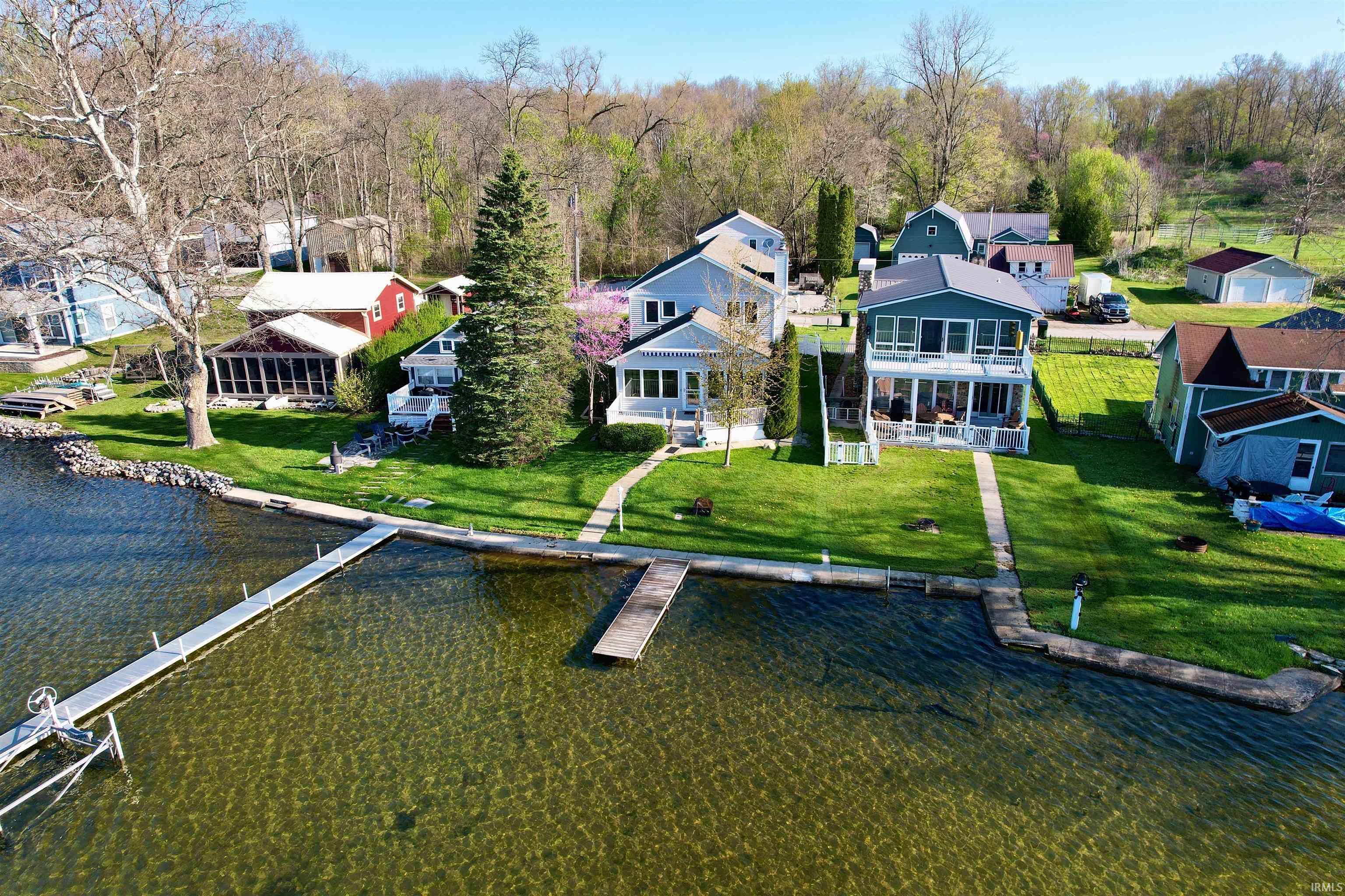 Image 1: Lakefront property featuring a private dock, lush green lawn, mature trees, and a concrete pathway leading to the water's edge, Aerial View