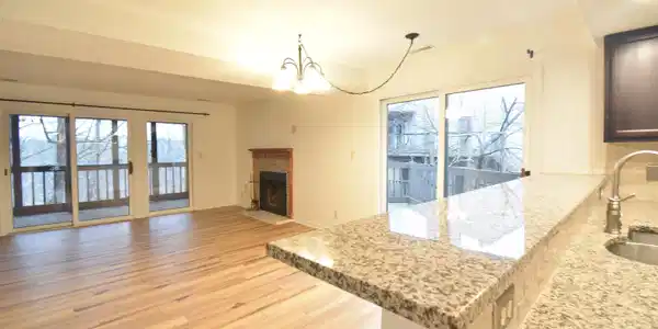 Image 1: Kitchen featuring light stone countertops, hanging lights, a fireplace with flush hearth, light wood-style floors, and plenty of natural light, Great Room Image 1: Kitchen featuring light stone countertops, hanging lights, a fireplace with flush hearth, light wood-style floors, and plenty of natural light, Great Room