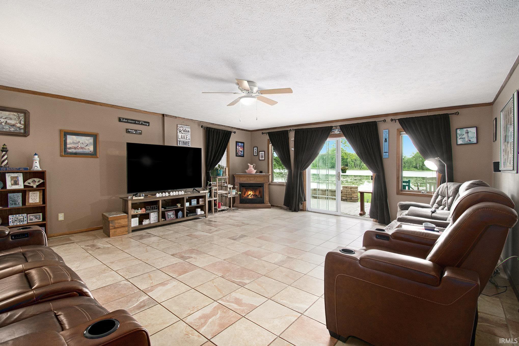 Image 2: Living room with crown molding, ceiling fan, a warm lit fireplace, a textured ceiling, and light tile patterned floors, Living Room