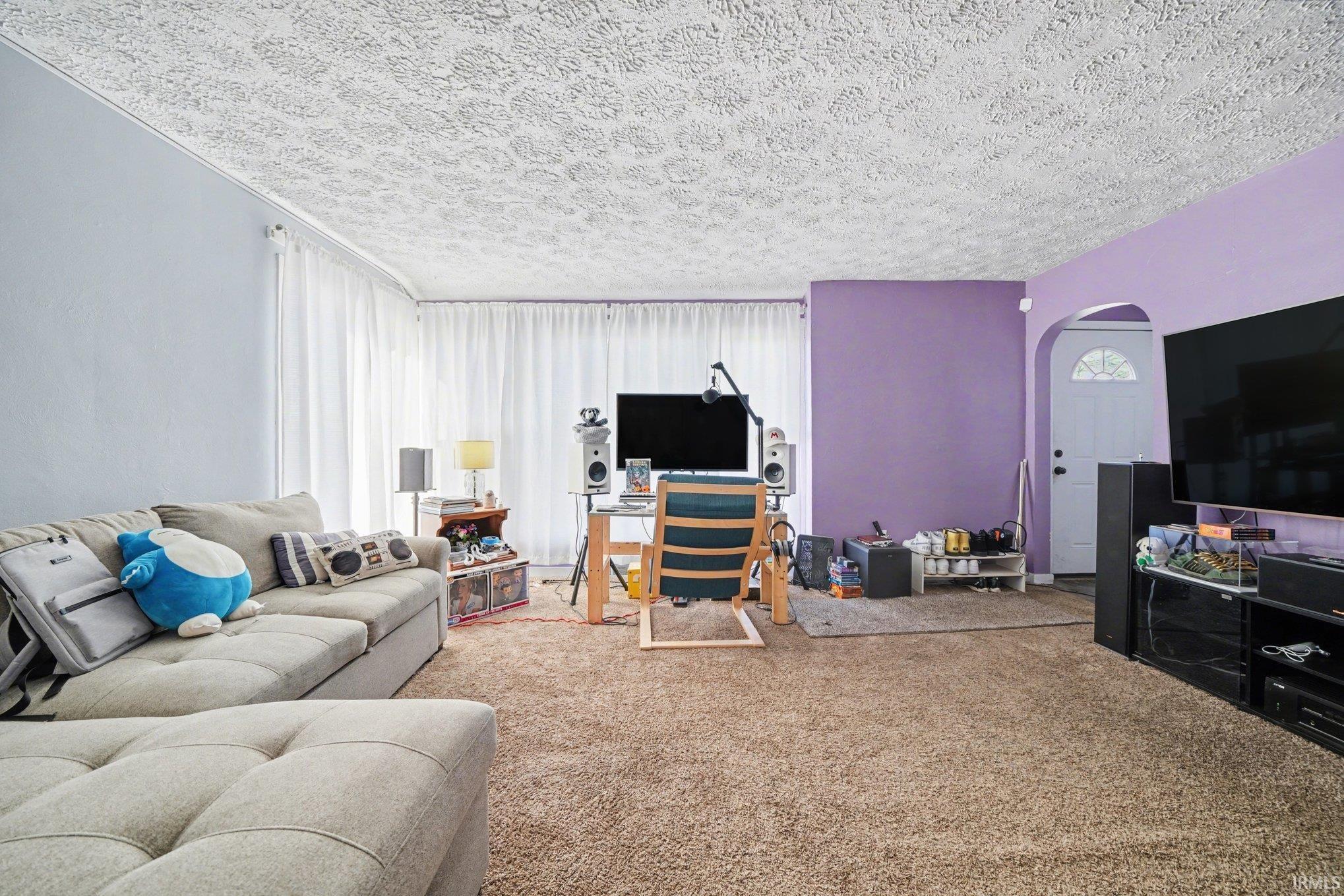 Image 2: Carpeted living area with arched walkways and a textured ceiling, Living Room