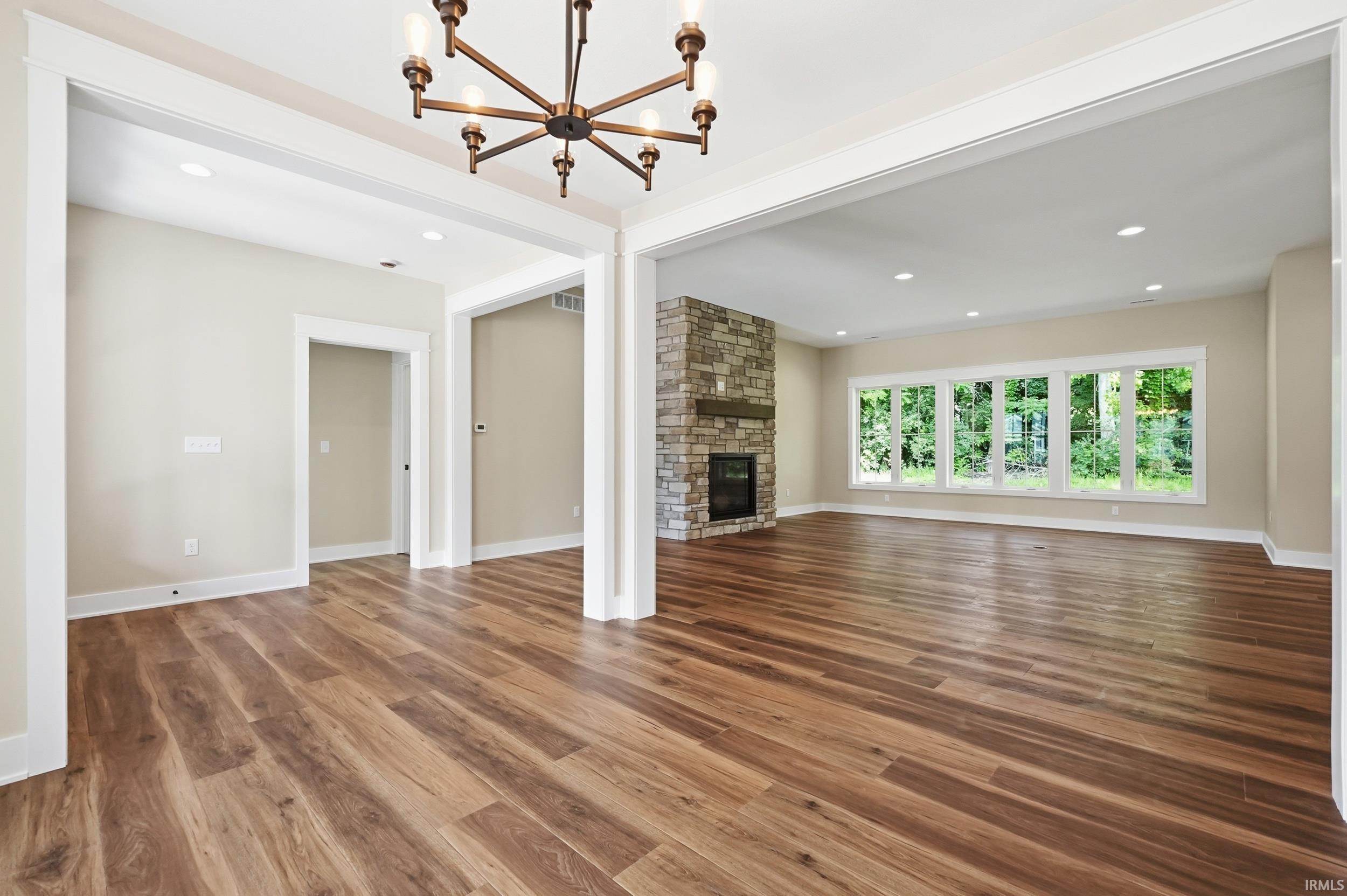 Image 2: Spacious interior featuring wood-finish flooring, a stone-faced fireplace with a wood mantel, and multiple large windows, Living Room