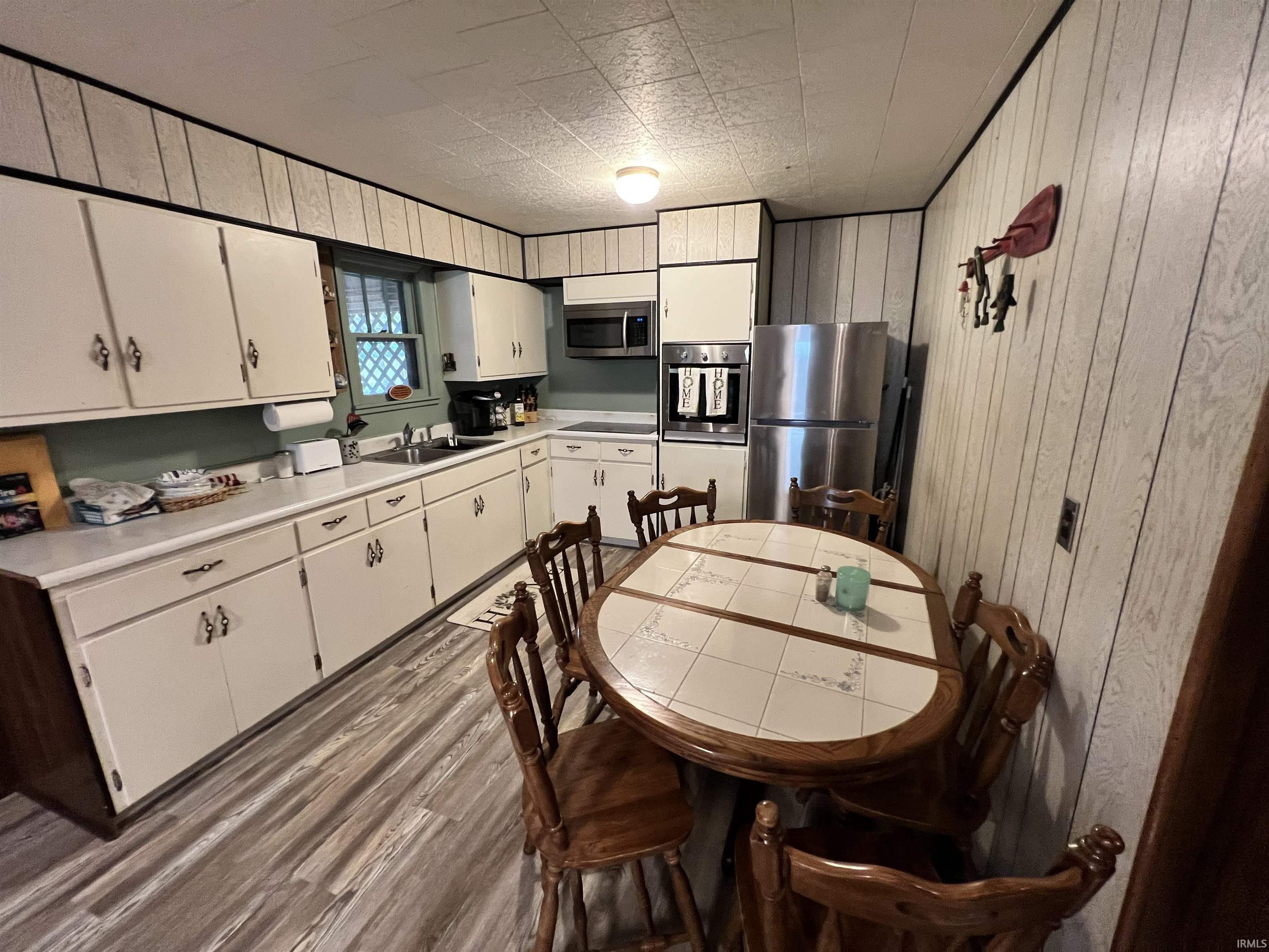 Image 1: Kitchen featuring white cabinetry, wood-finish flooring, a stainless steel refrigerator, and a built-in oven with microwave, Kitchen Image 1: Kitchen featuring white cabinetry, wood-finish flooring, a stainless steel refrigerator, and a built-in oven with microwave, Kitchen