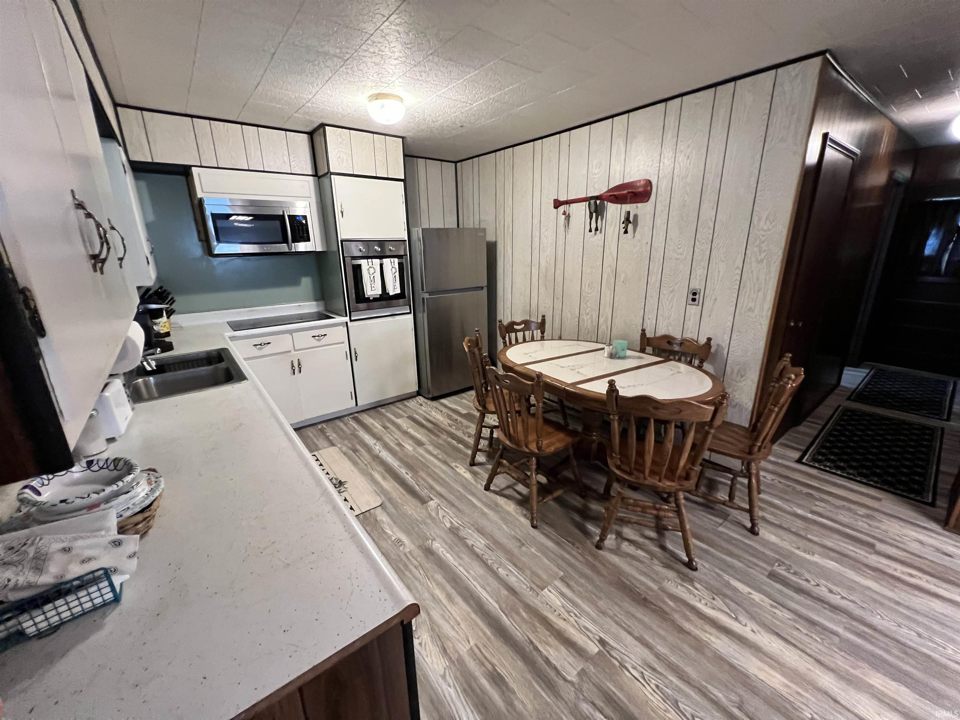 Image 2: Kitchen area featuring wood-finish flooring, white cabinetry, integrated stainless steel microwave, built-in wall oven, and a stainless steel refrigerator, Kitchen Image 2: Kitchen area featuring wood-finish flooring, white cabinetry, integrated stainless steel microwave, built-in wall oven, and a stainless steel refrigerator, Kitchen