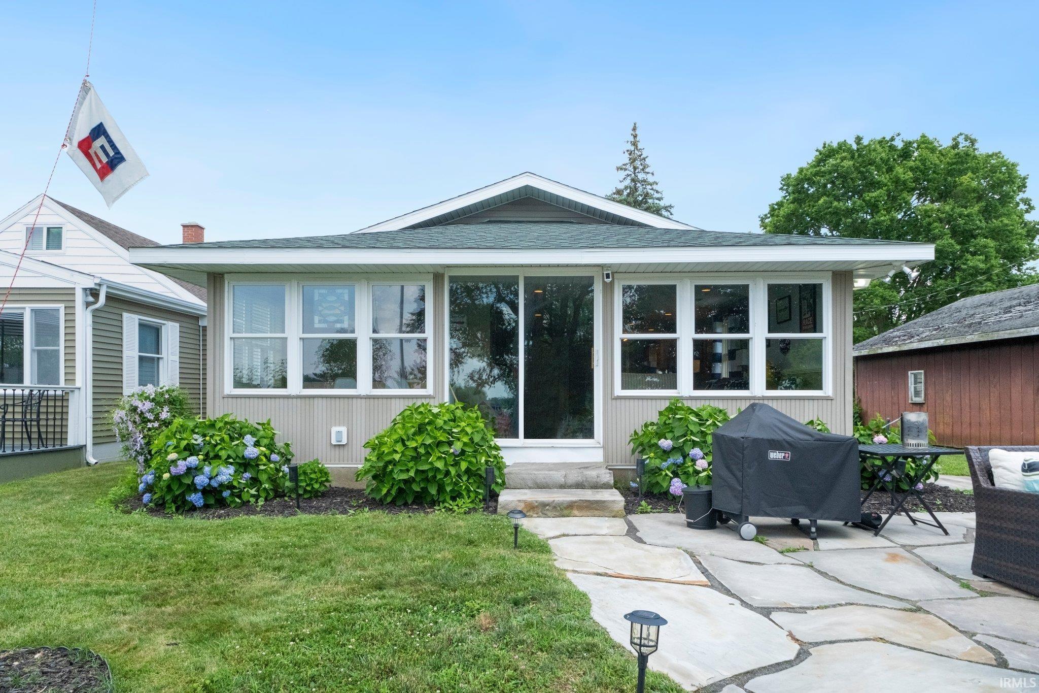 Image 0: Rear exterior featuring a sliding glass door entry, multiple windows, and a stone patio, Back Of Structure Image 0: Rear exterior featuring a sliding glass door entry, multiple windows, and a stone patio, Back Of Structure