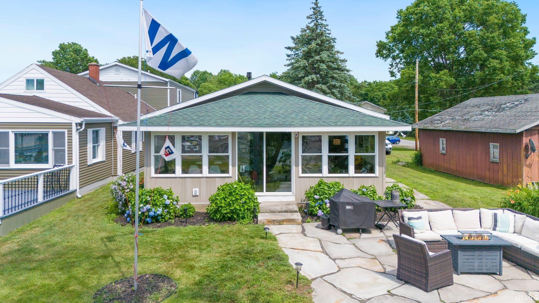 Image 3: Front exterior with a green shingle roof, light-colored siding, and a stone patio, Back Of Structure Image 3: Front exterior with a green shingle roof, light-colored siding, and a stone patio, Back Of Structure