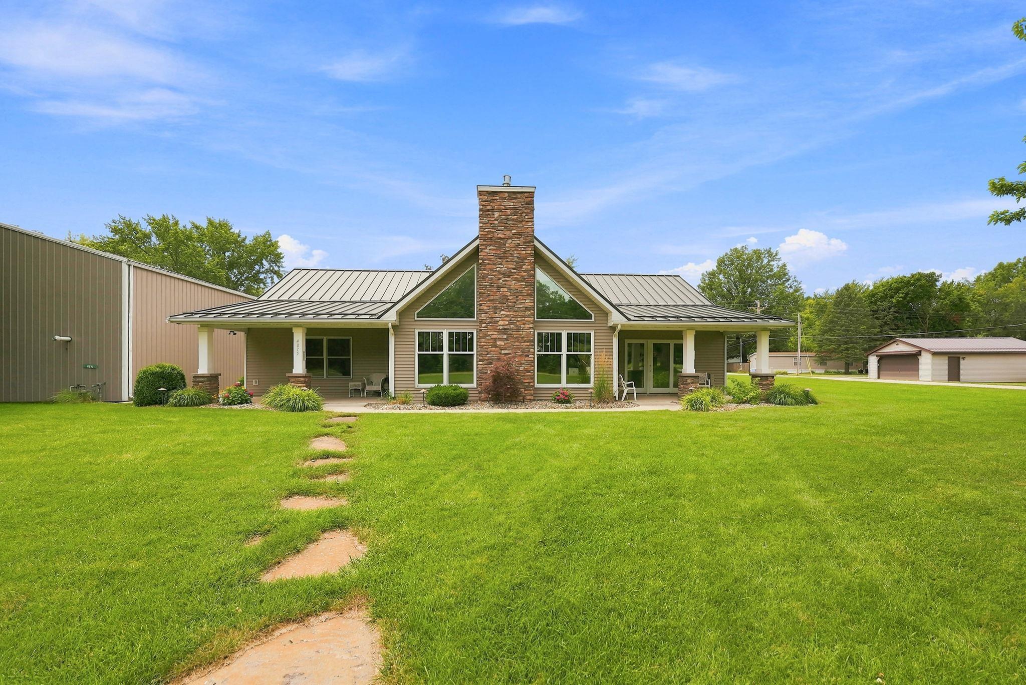 Image 1: Contemporary residence featuring a prominent stone chimney, a covered front porch with white columns, and a metal roof, Back Of Structure Image 1: Contemporary residence featuring a prominent stone chimney, a covered front porch with white columns, and a metal roof, Back Of Structure